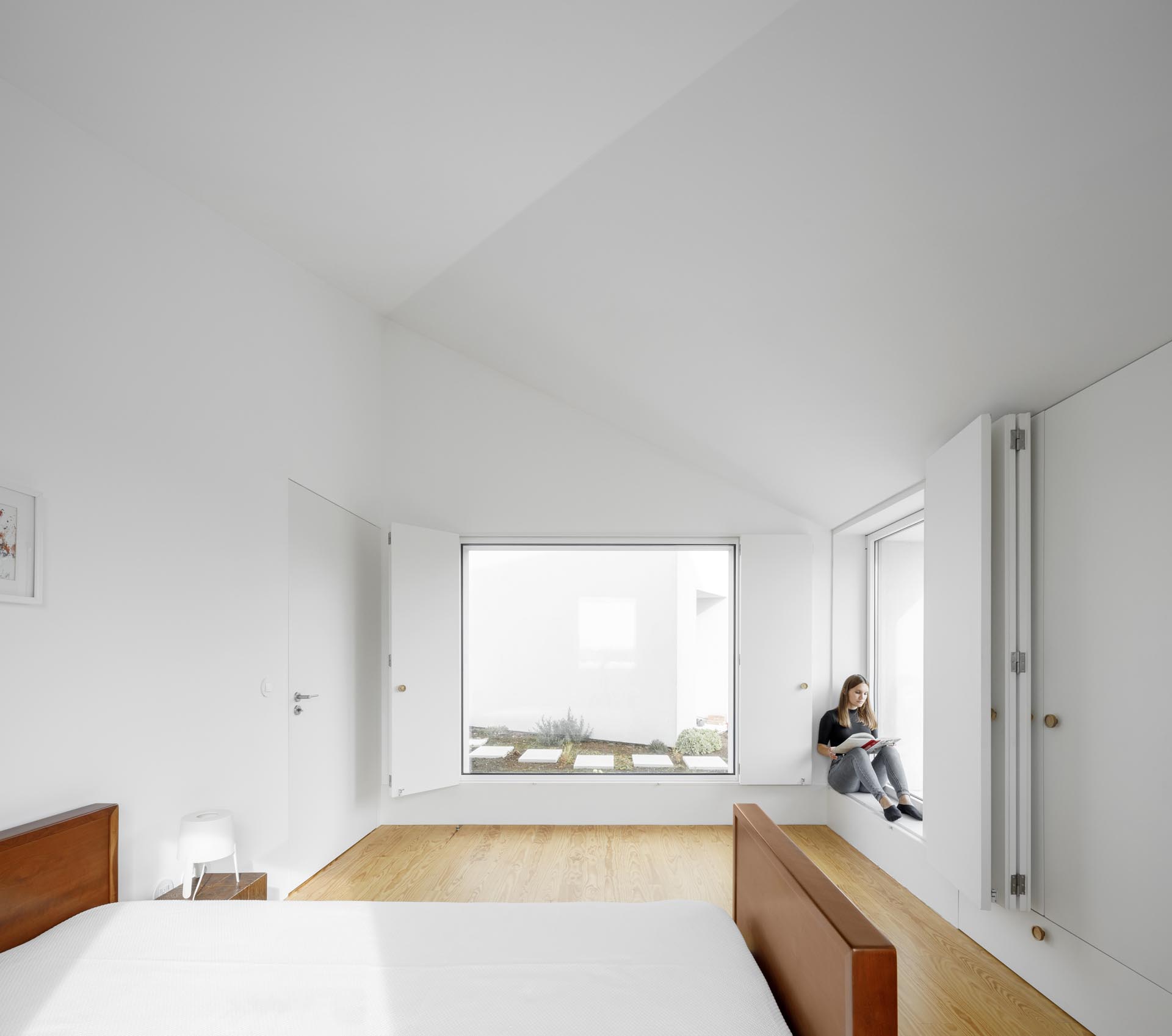 A modern bedroom with minimalist furnishings and folding window shutters.