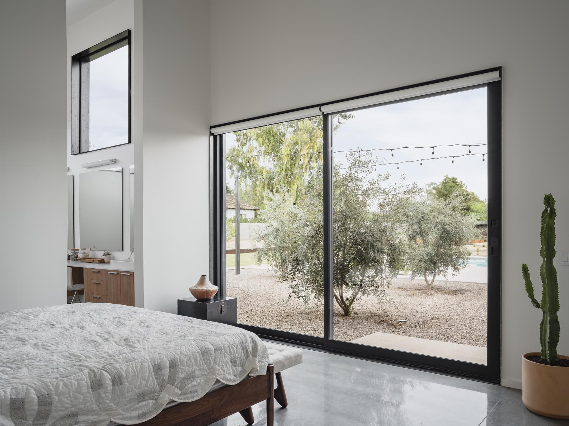 In this modern master bedroom, high ceilings create a lofty and open room, while a sliding door connects to the outdoors. 