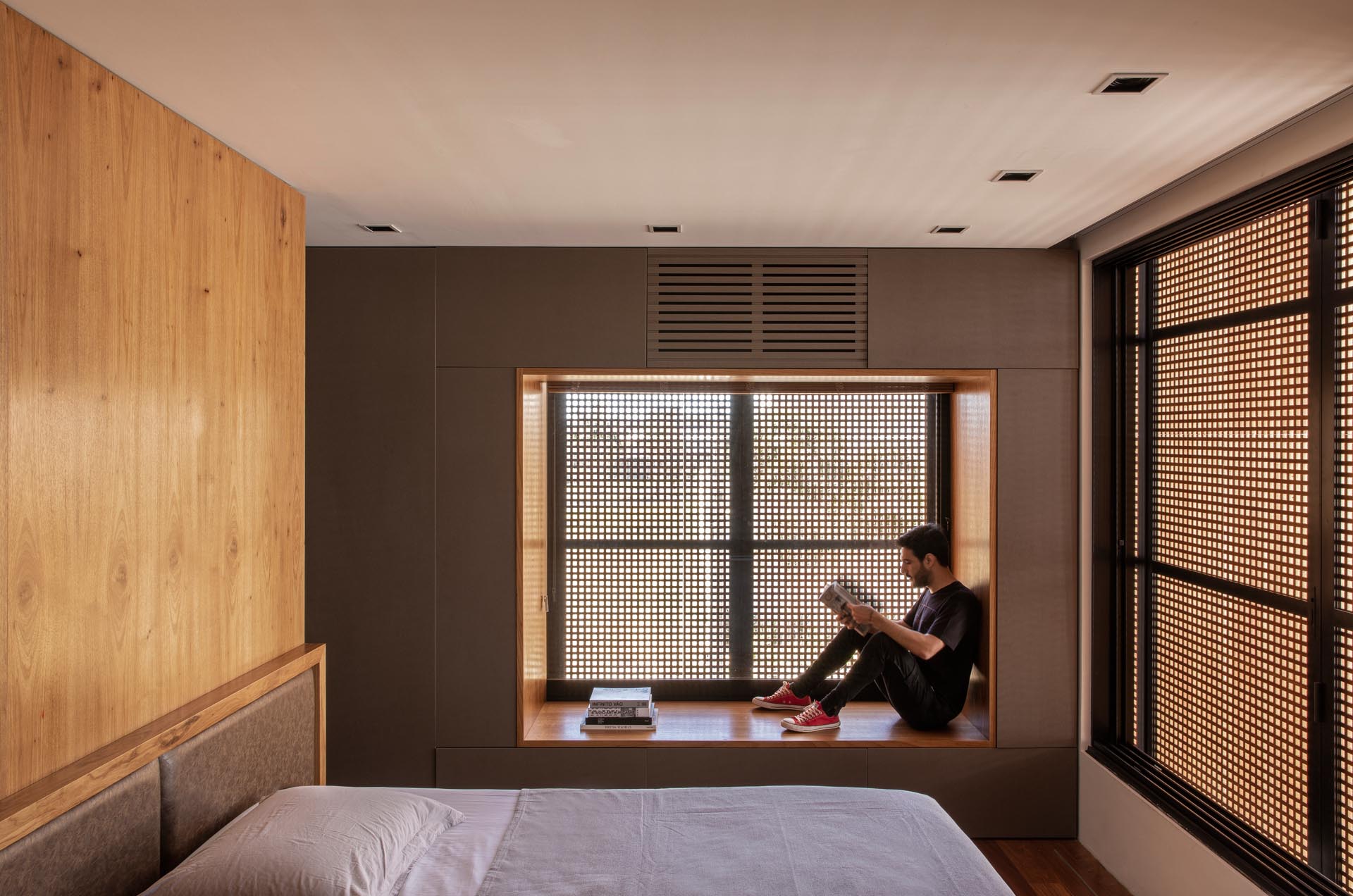 In this modern bedroom, there's a wood lined window seat that acts as a small reading nook. The louvers on the exterior of the home provide shade and privacy without blocking the natural light.