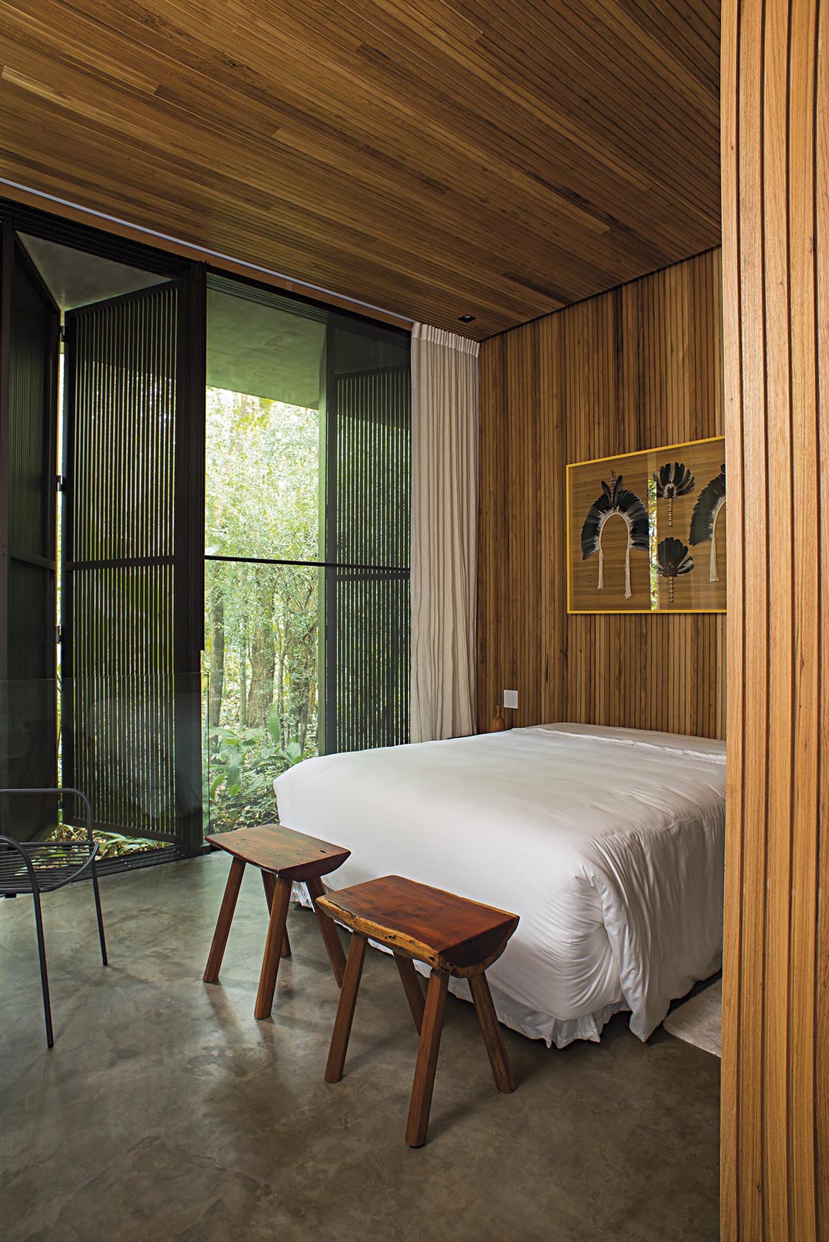 In this modern bedroom the wood ceiling carries on to the wall, creating a backdrop for the bed and artwork. Wood shutters create privacy, however when open, they allow the natural light to flood the room.