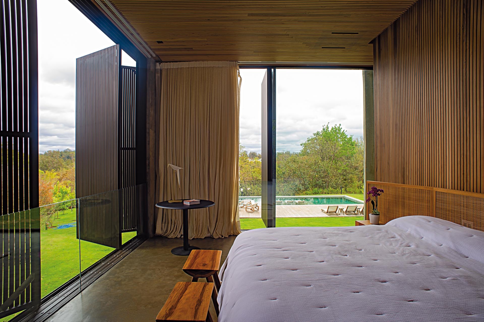 the wood ceiling carries on to the wall, creating a backdrop for the bed and artwork. Wood shutters create privacy, however when open, they allow the natural light to flood the room.