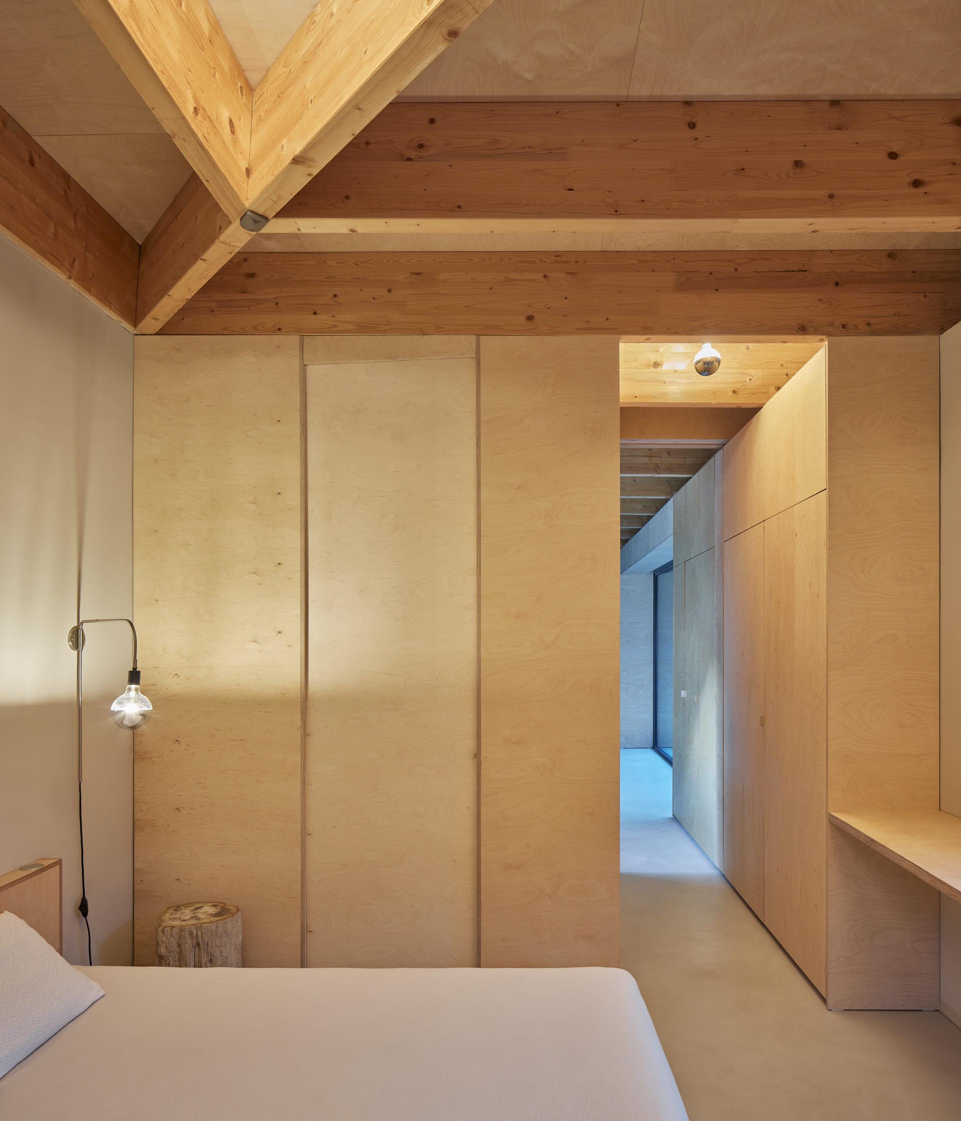 Plywood closets line the hallway that leads to a bedroom, which is minimally furnished.