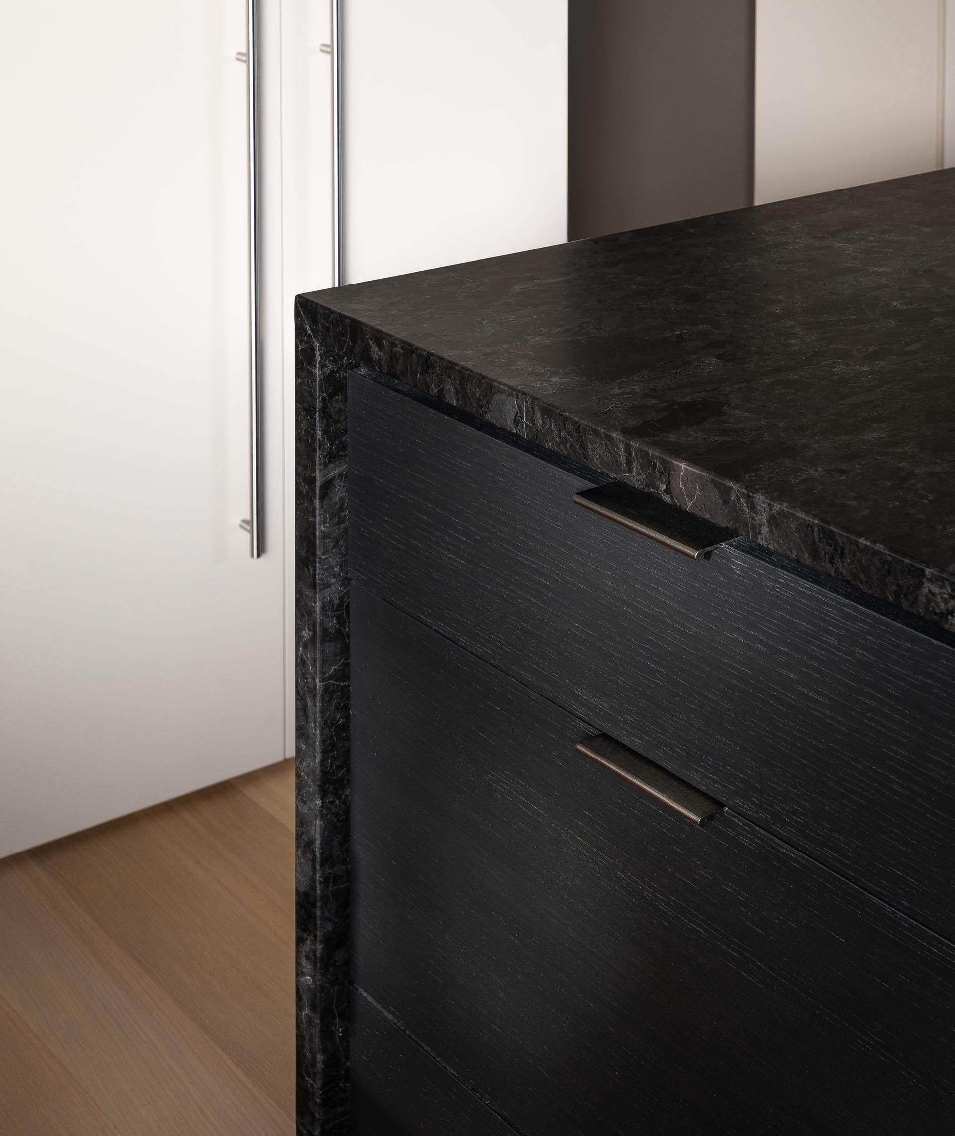 A modern kitchen with wood floors, white cabinets, and a black island.