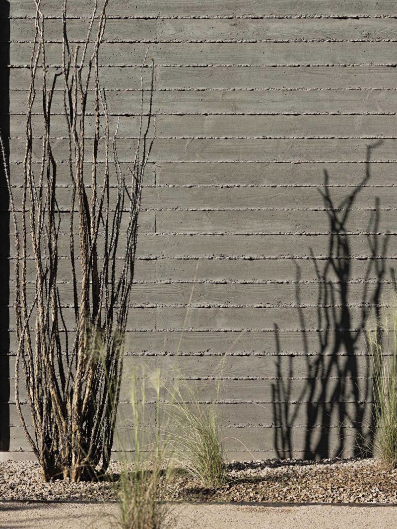 A modern home with board formed concrete walls and desert landscaping.