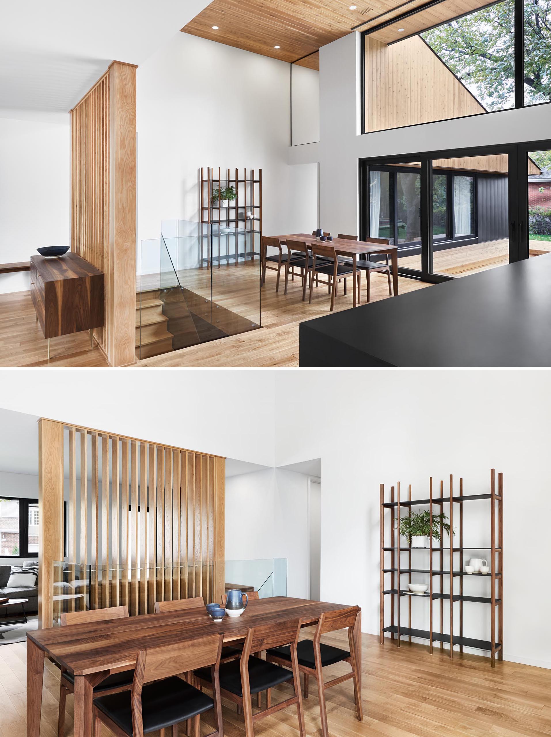 A modern dining room with high ceilings, glass stair railings, and a wood partition screen.