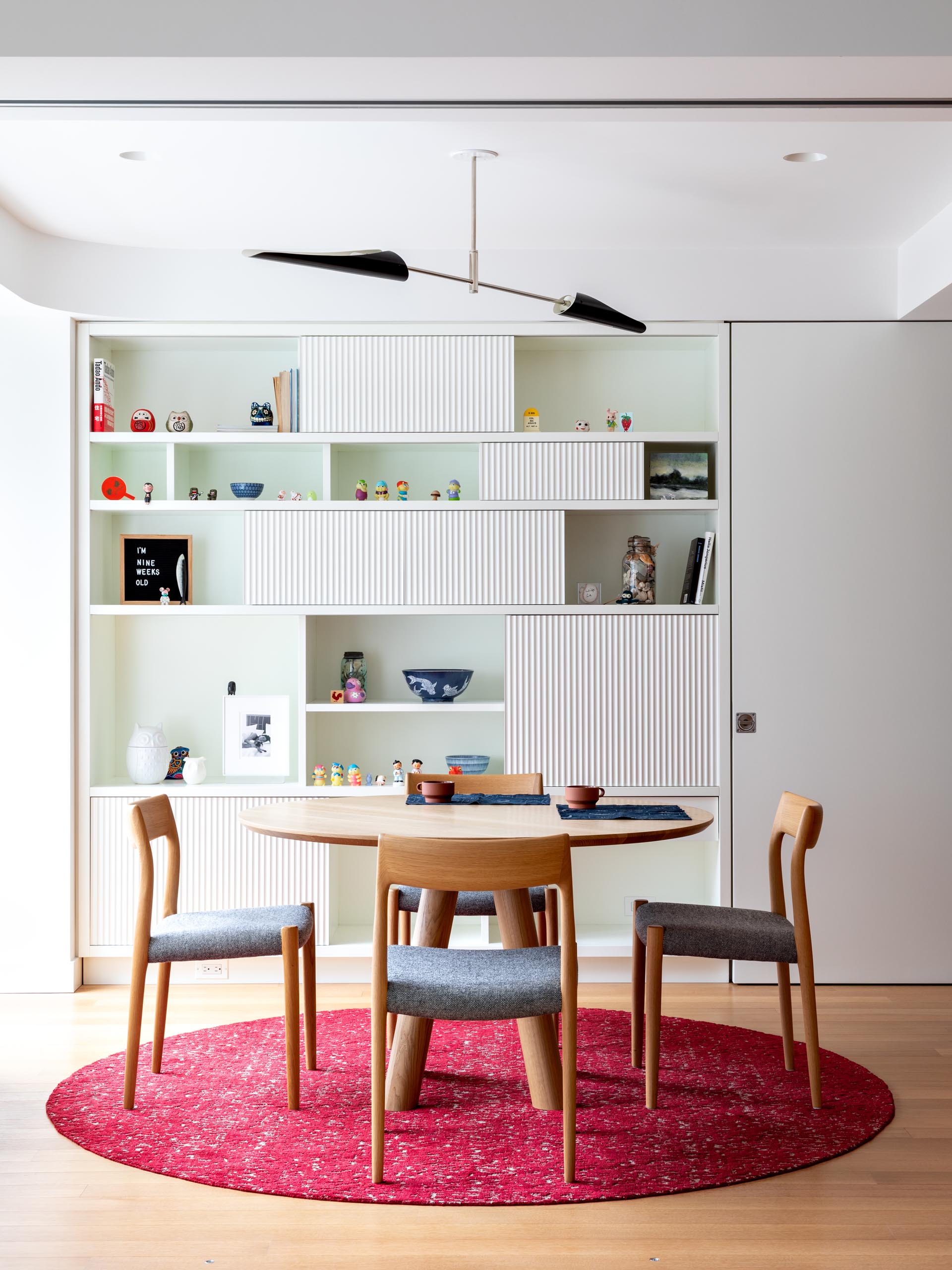 This modern dining room has a large bookshelf with textured panes that's used for displaying decorative items.