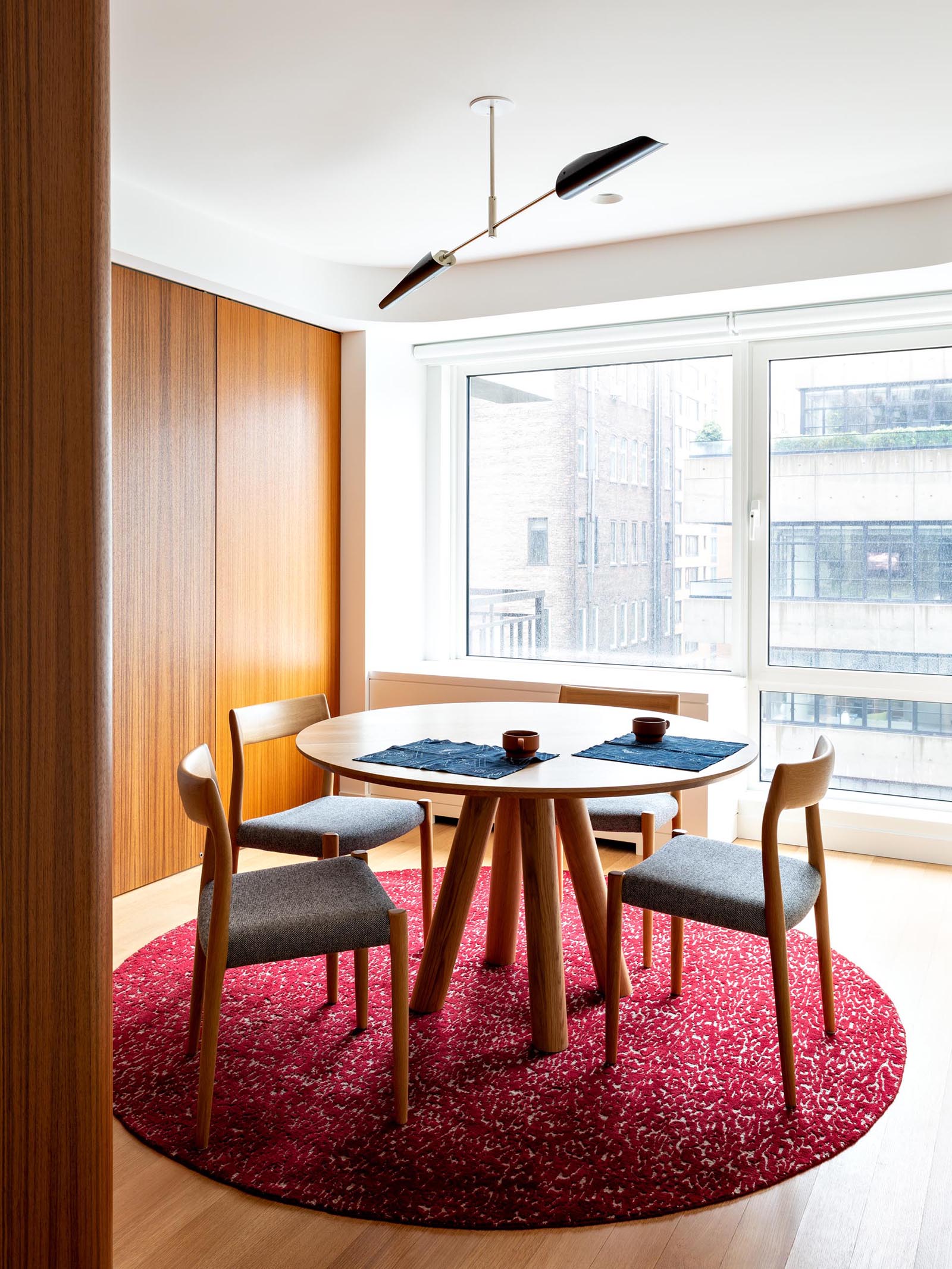 A modern dining room with a colorful burgundy/pink rug with wood furniture.