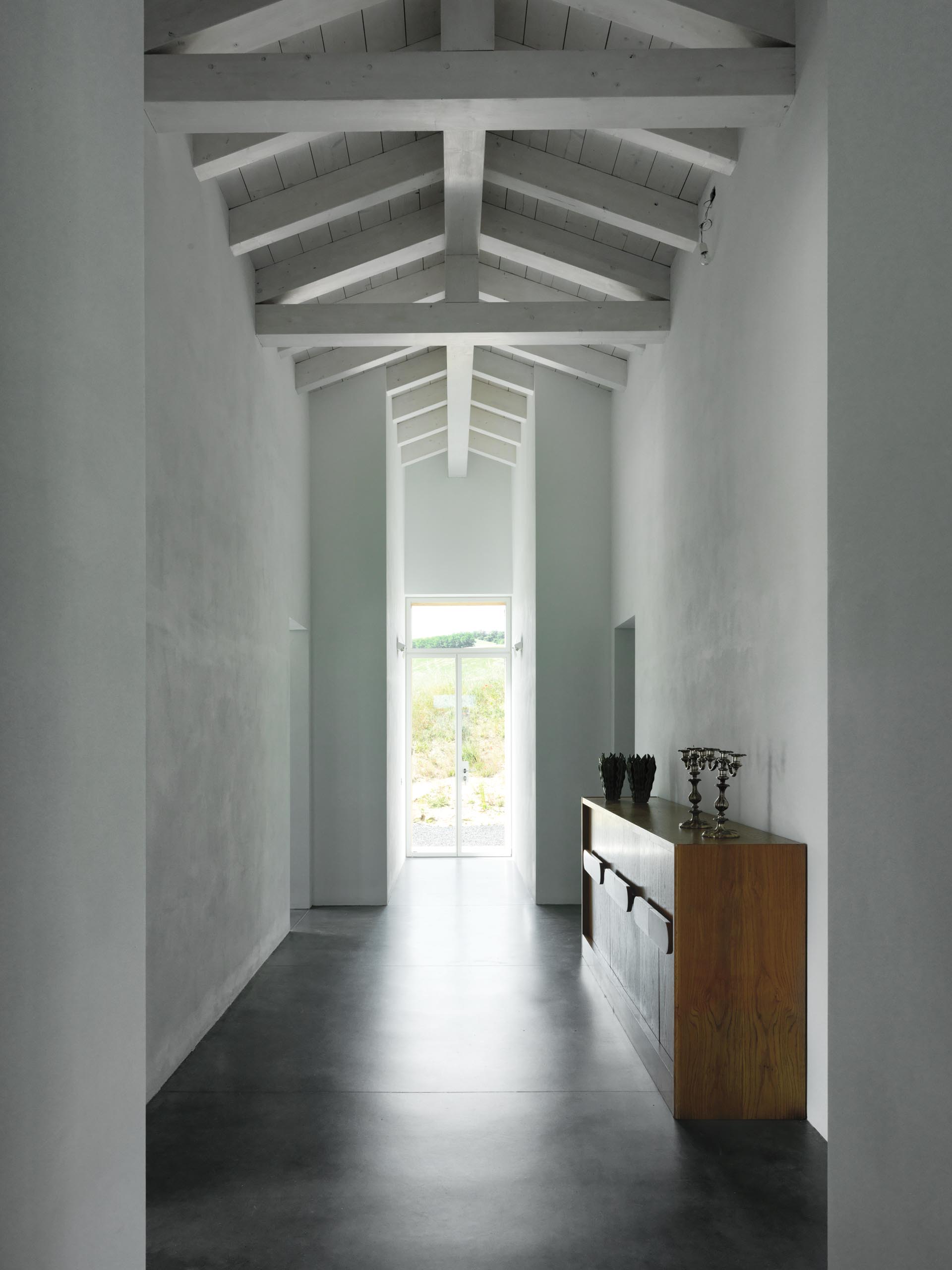 A modern farmhouse hallway with white lime tempera walls and concrete floors.