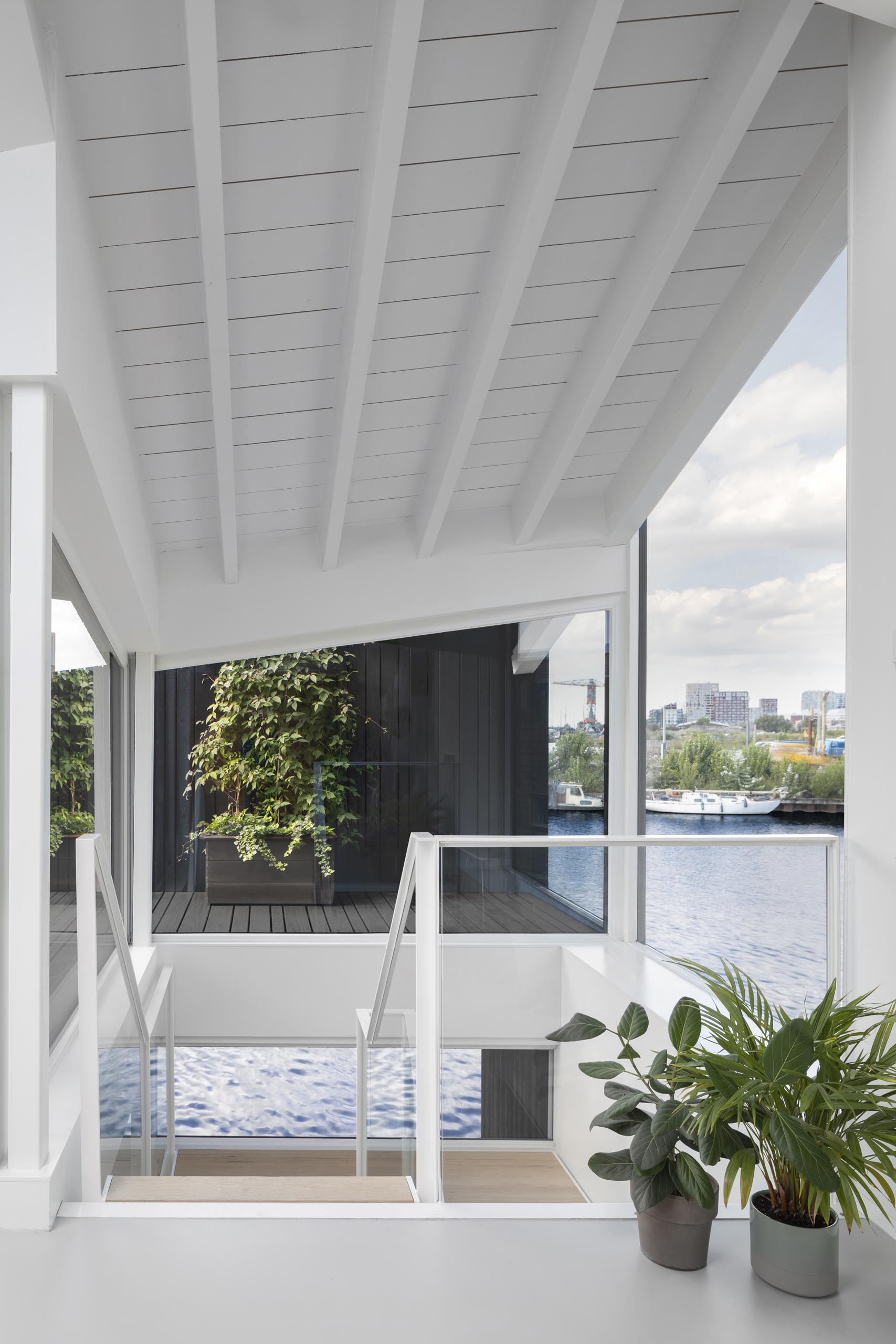 A white staircase in this modern float home matches the walls and ceiling, connects the various levels of the float home, and adds a warm wood element to the space.