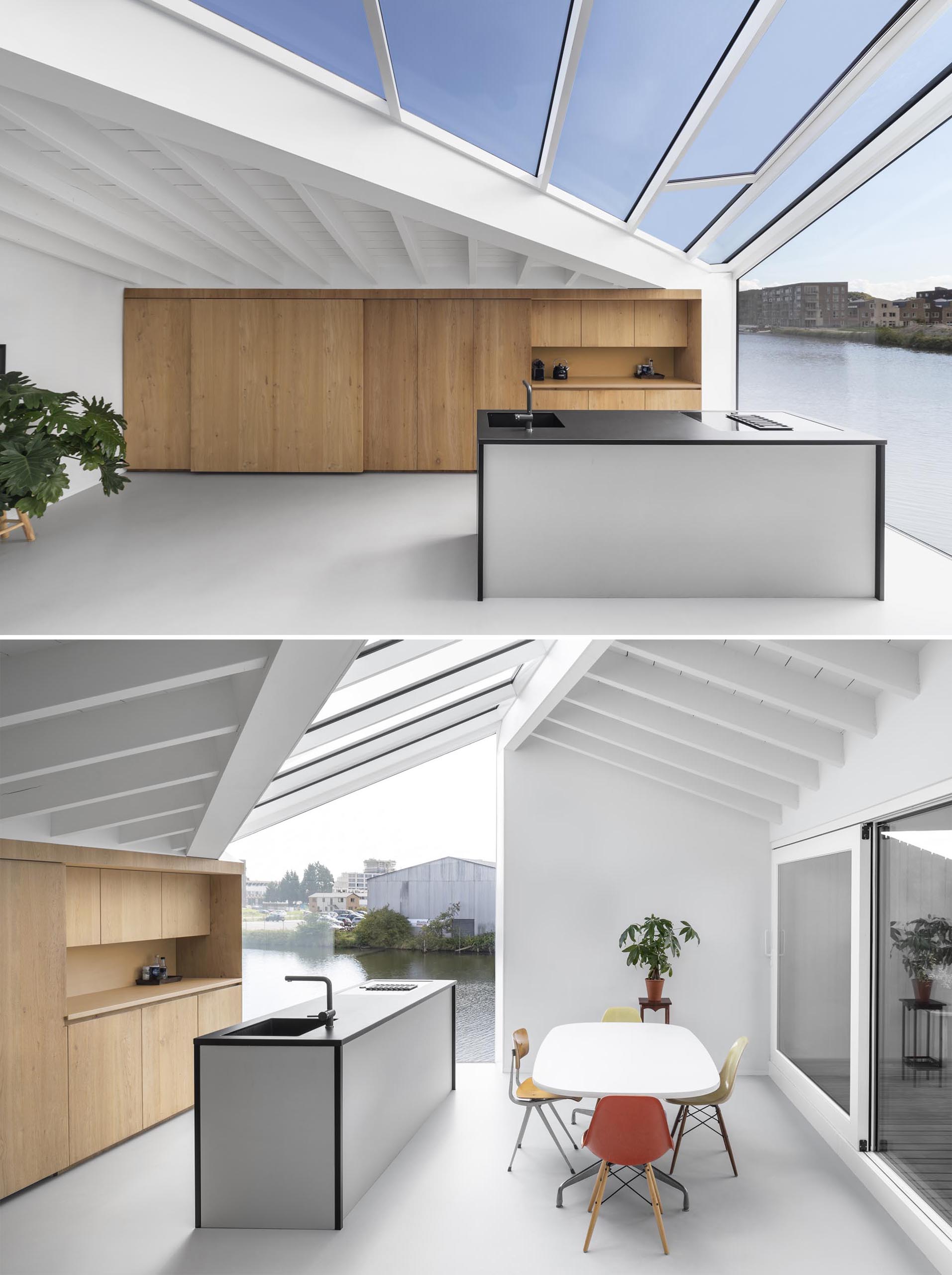 In the kitchen of a modern float home, a wall of wood cabinets is complemented by an island with a black countertop. An abundance of windows helps to keep the interior bright and open.