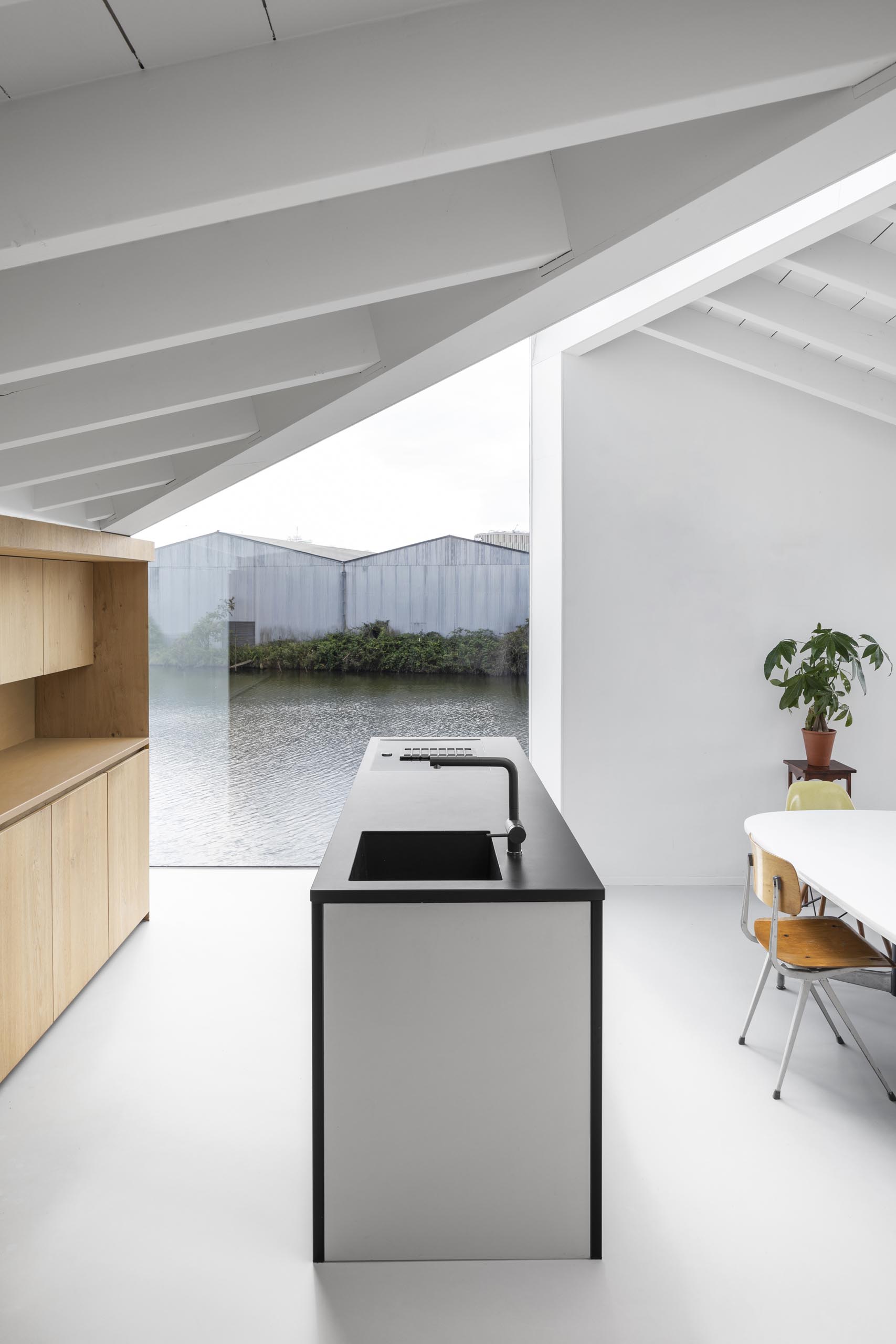 In the kitchen of a modern float home, a wall of wood cabinets is complemented by an island with a black countertop. An abundance of windows helps to keep the interior bright and open.