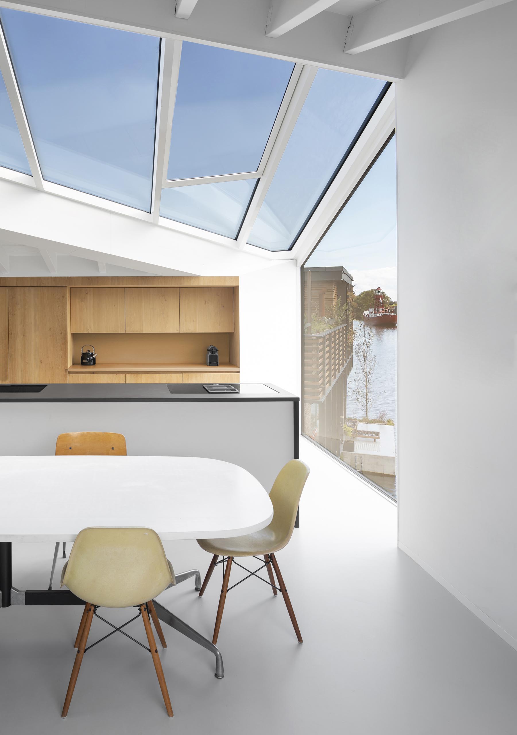 In the kitchen of a modern float home, a wall of wood cabinets is complemented by an island with a black countertop. An abundance of windows helps to keep the interior bright and open.