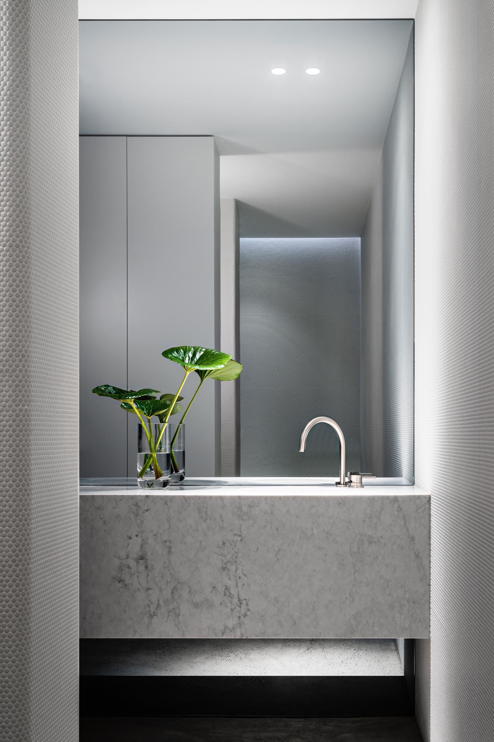 A modern bathroom with a marble vanity and penny tile walls.