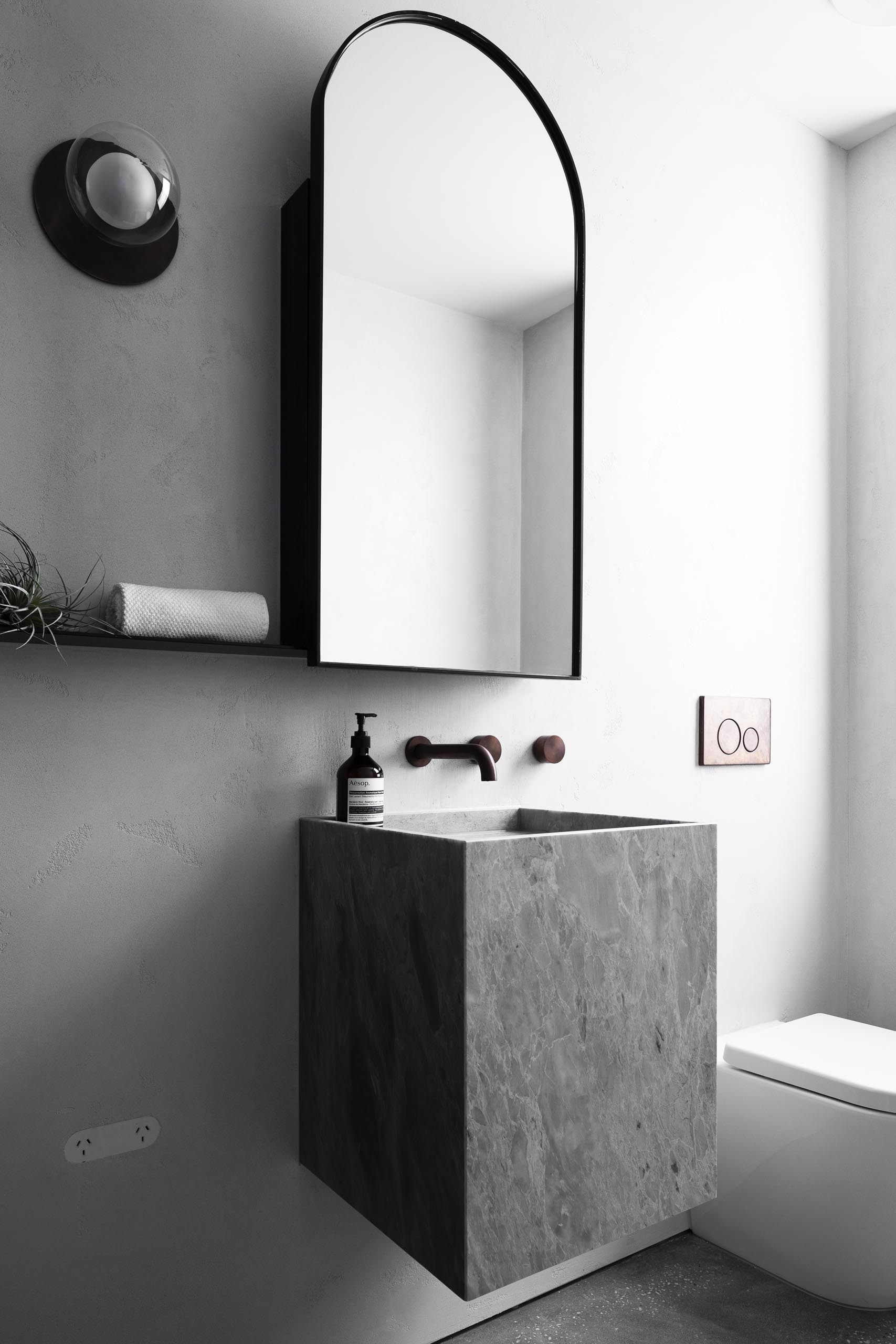 A gray bathroom with a black framed arched mirror and floating vanity.