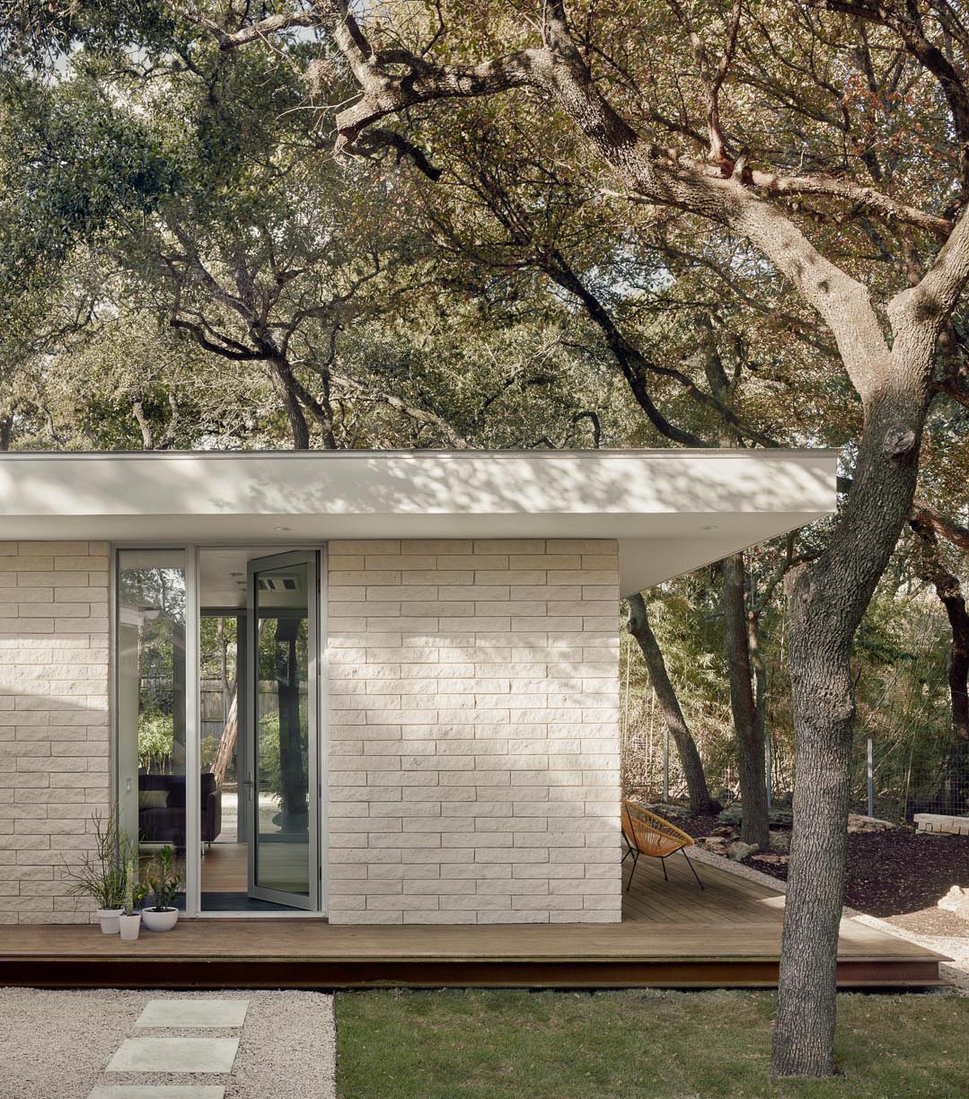 A wood deck surrounds a small modern house, while a glass door welcomes people inside.