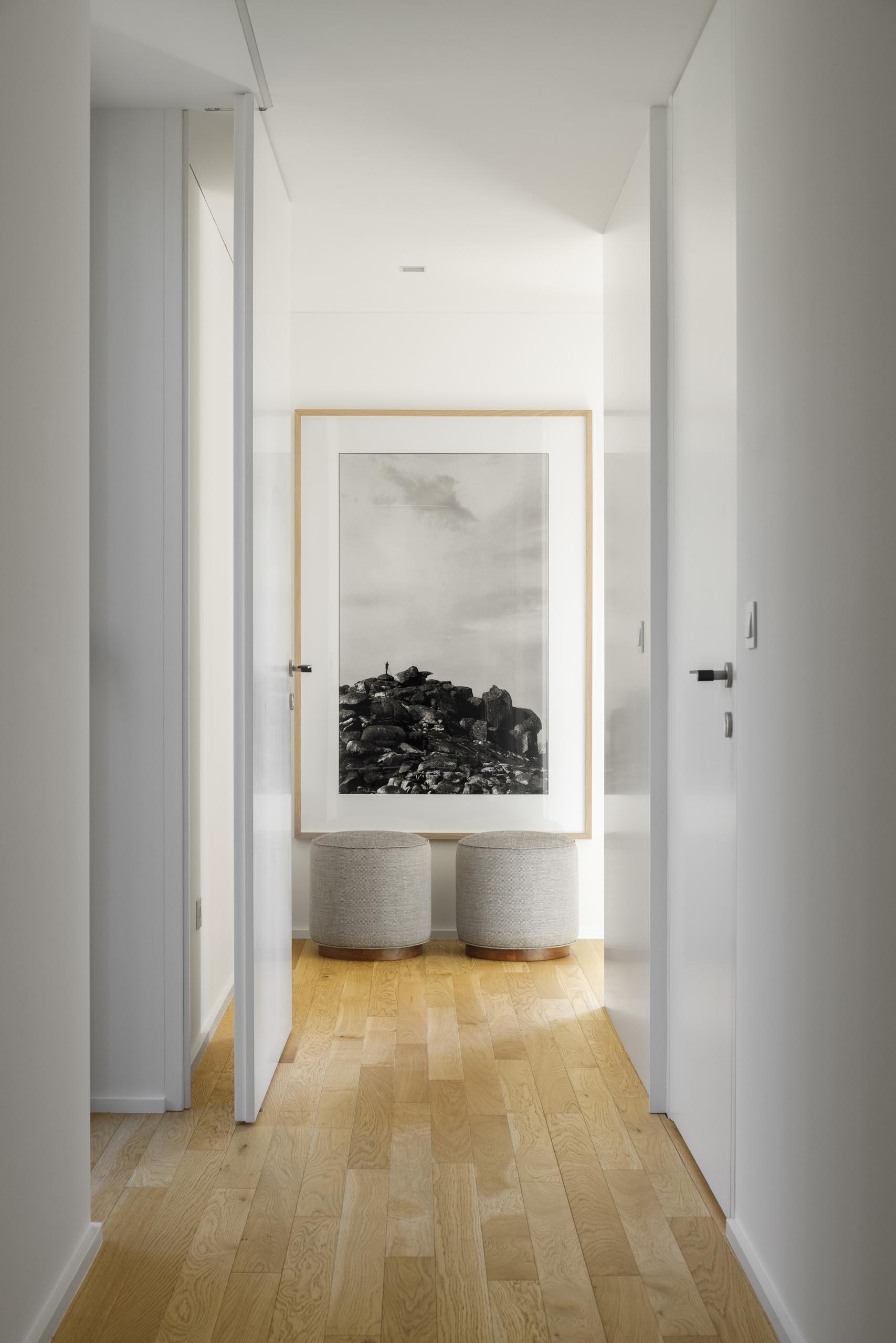 A modern white hallway with wood floors and a large vertical art print.