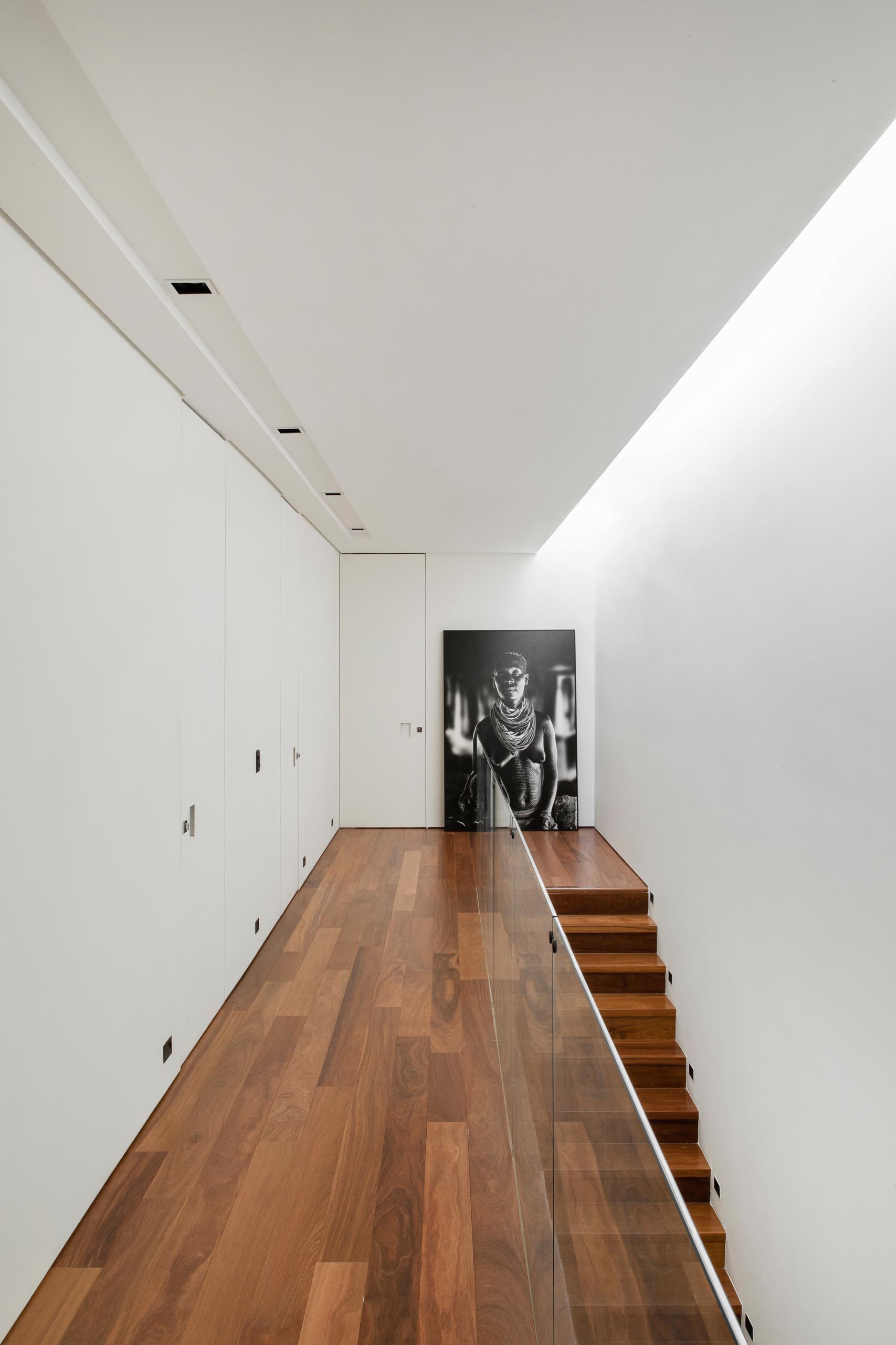 A modern house with wood stairs that match the flooring, while a glass railing allows natural light to filter throughout the interior from the skylight above.