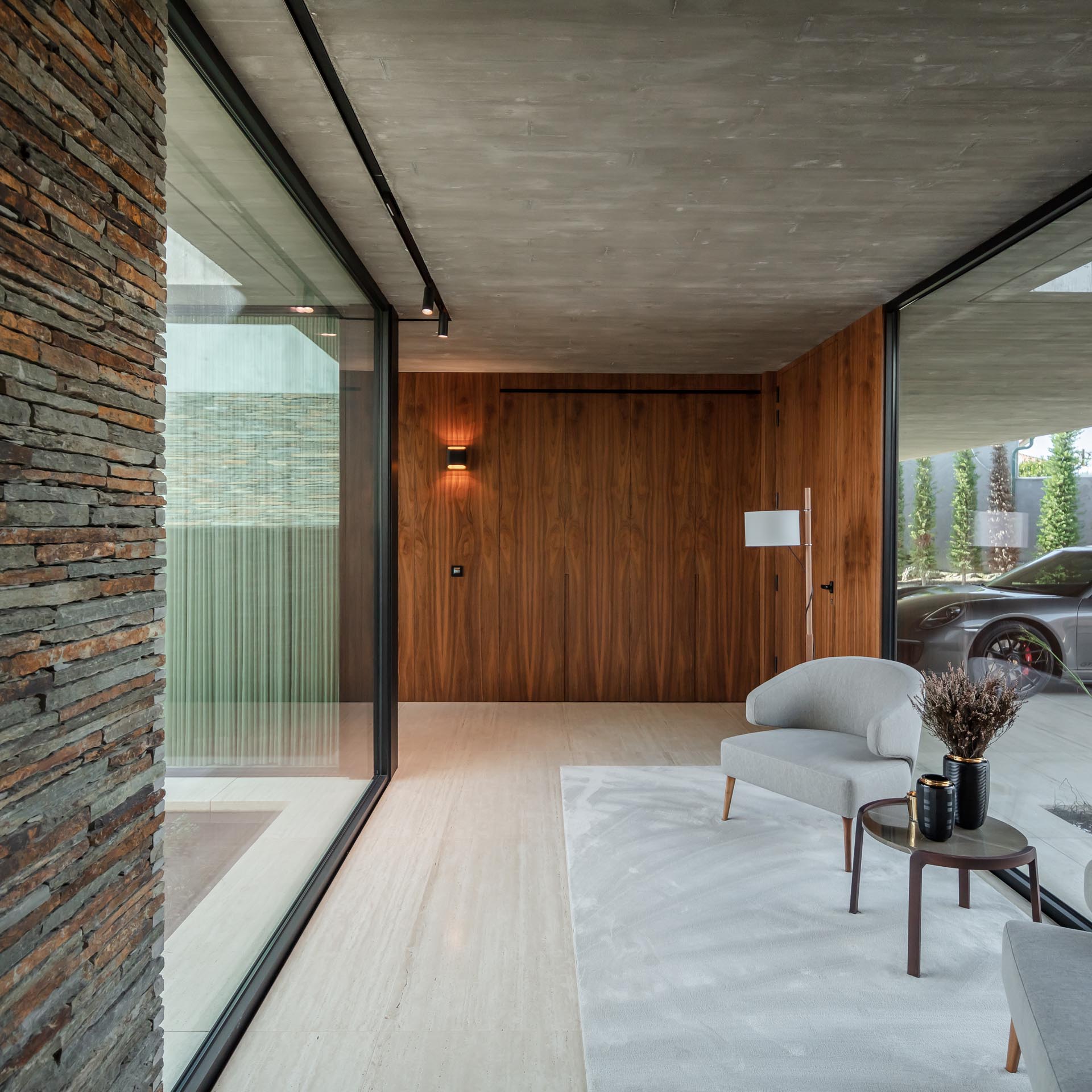 A modern entryway includes a small sitting area with floor to ceiling glass walls on either side.