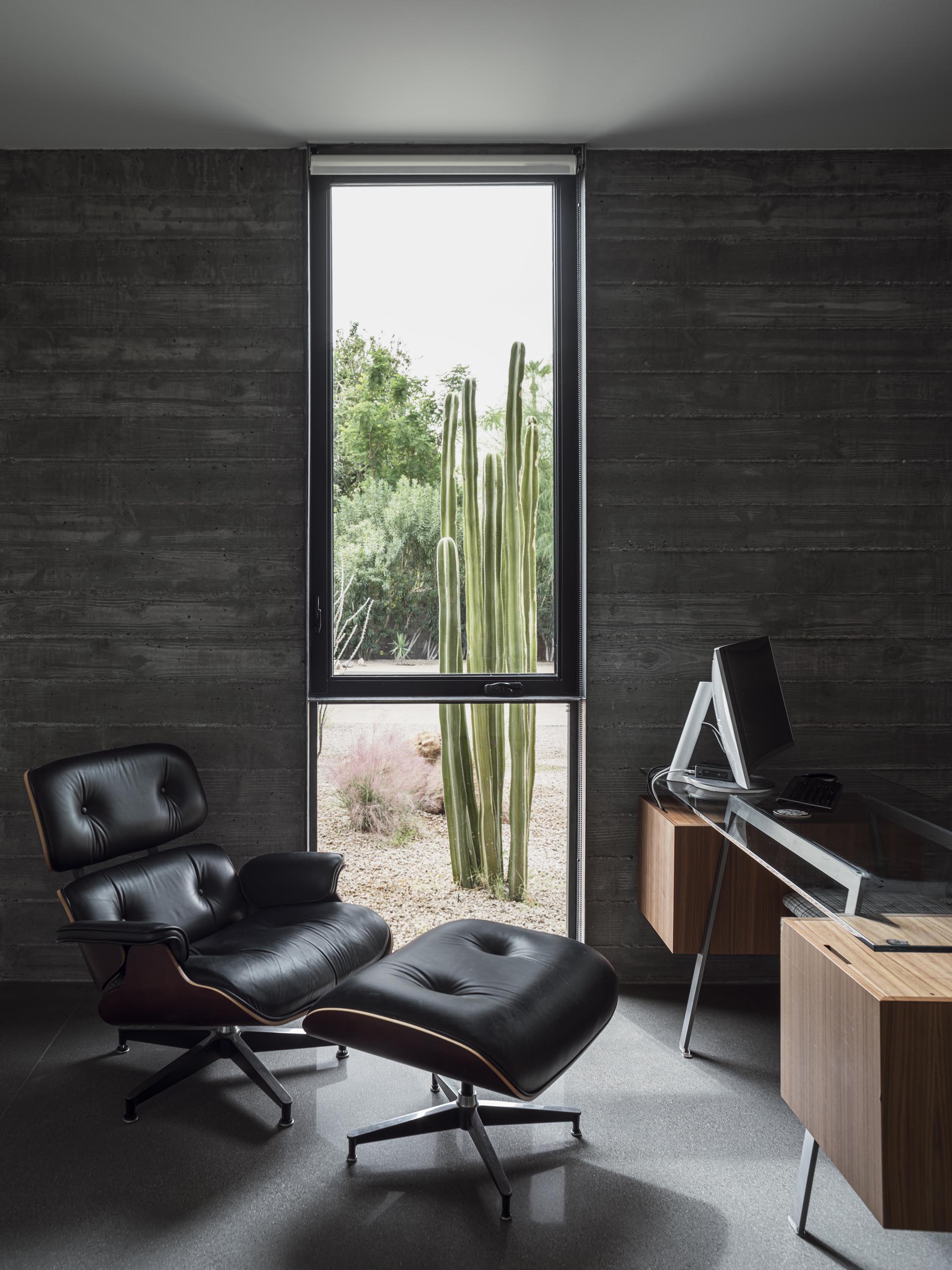 In this home office, the board formed concrete walls are clearly visible, while a floor-to-ceiling window perfectly frames the desert plants outside.