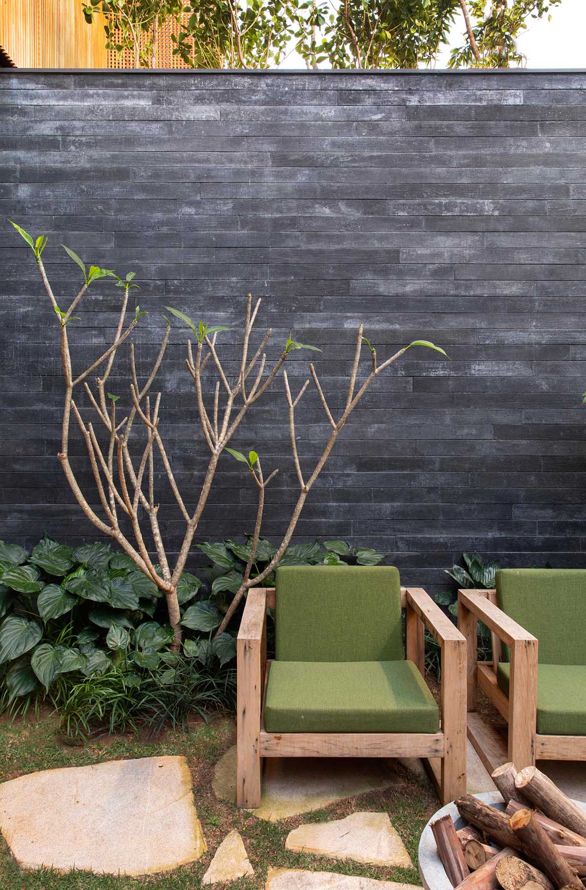 A modern landscaping design with a couple of wood armchairs, a flagstone patio, and fire bowl.