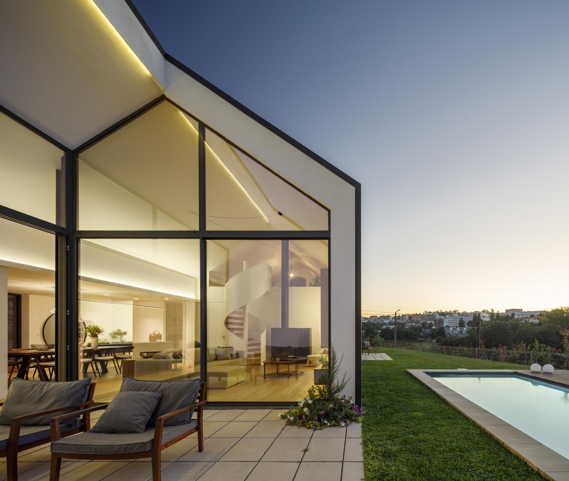 A modern house open to a small patio, the yard, and a swimming pool.