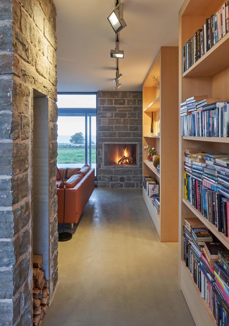 A contemporary summer home with limestone walls, concrete floors, and wood bookshelves.