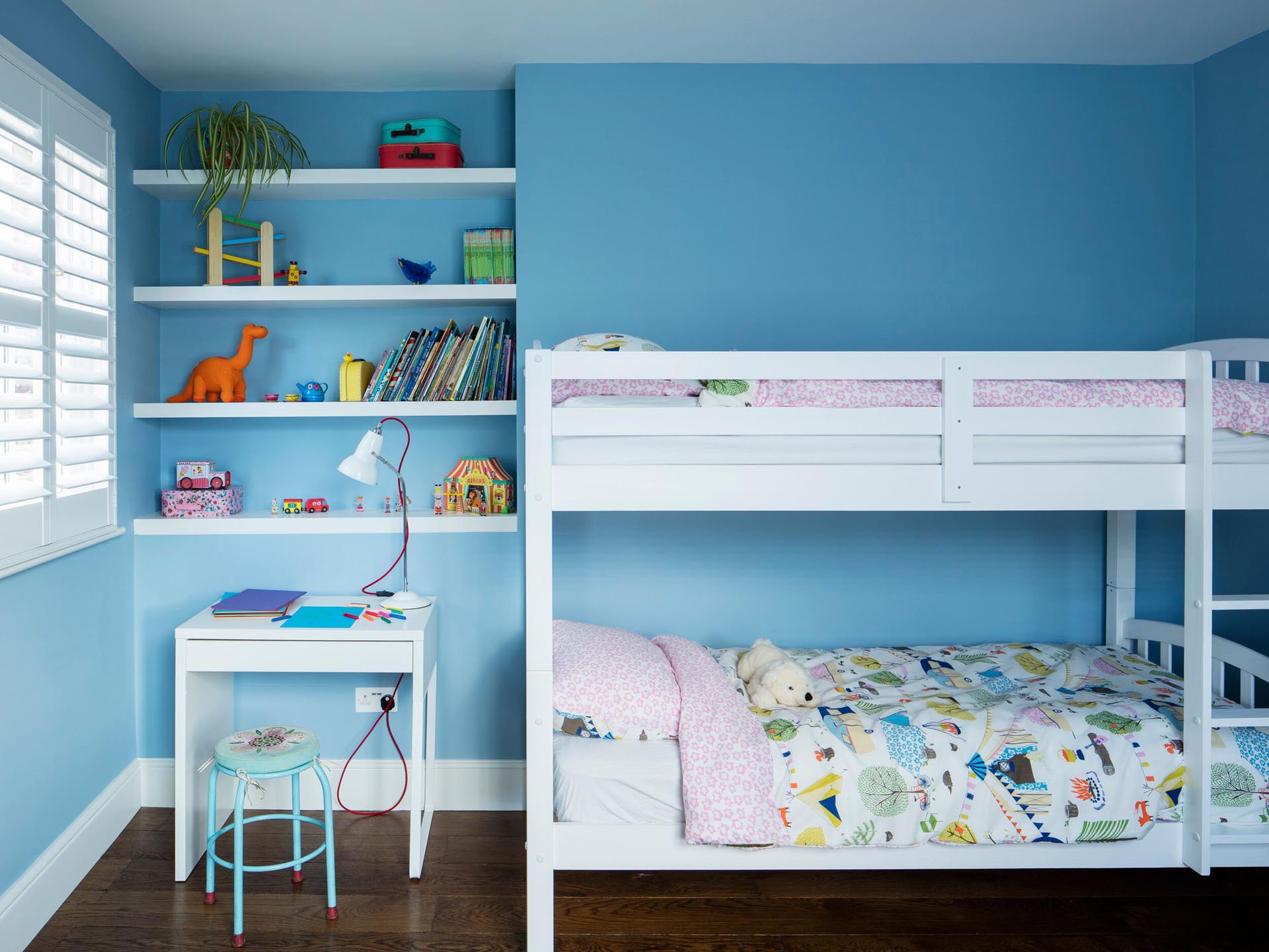 In this kids bedroom, bright blue walls create a colorful backdrop for white bunk beds, shelving, and a small desk.