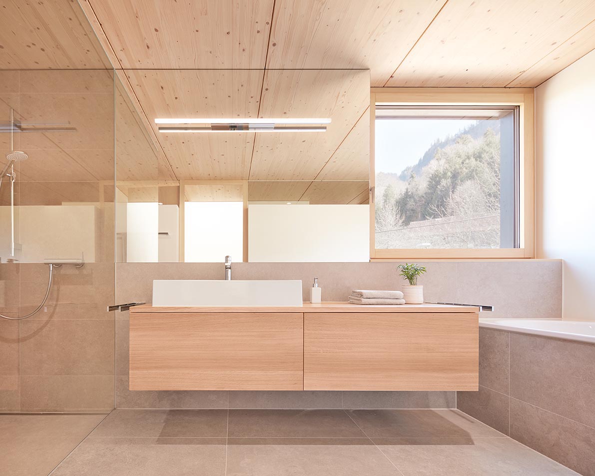 In this modern bathroom, a square window creates a picture perfect view of the trees, and the floating wood vanity separates the shower and the built-in bath.