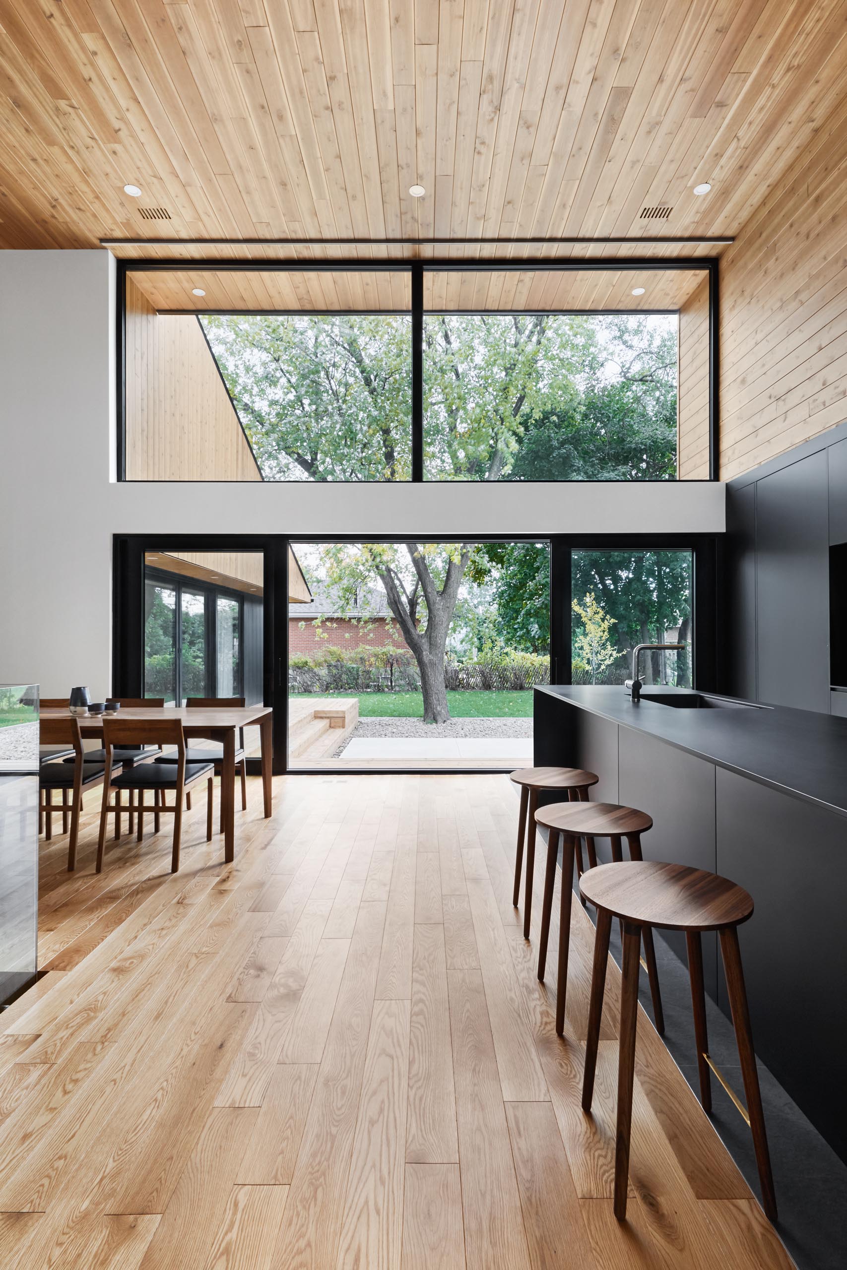 A modern home with high wood ceilings, large windows, a matte black kitchen, and open plan interior.