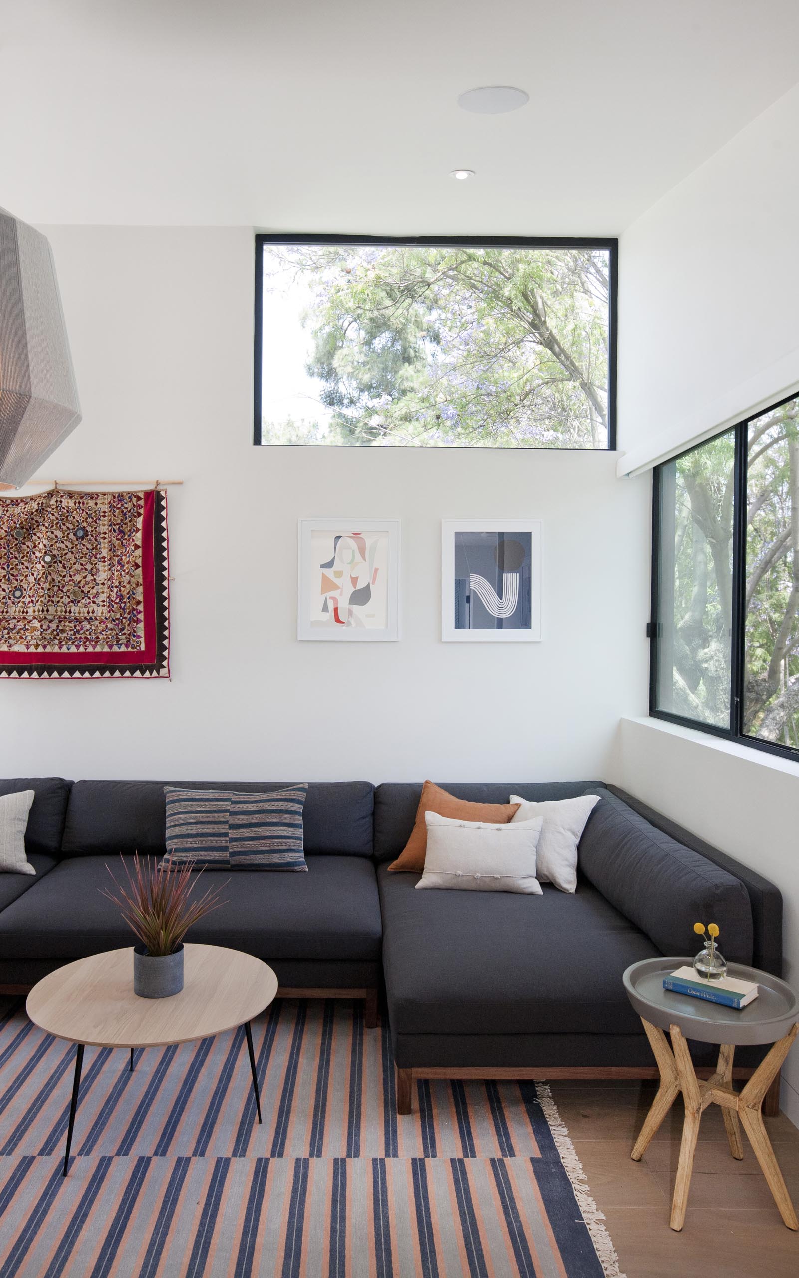 In his modern casual living / reading room, there's a dark gray sofa and a cabinet with open shelving filled with books.