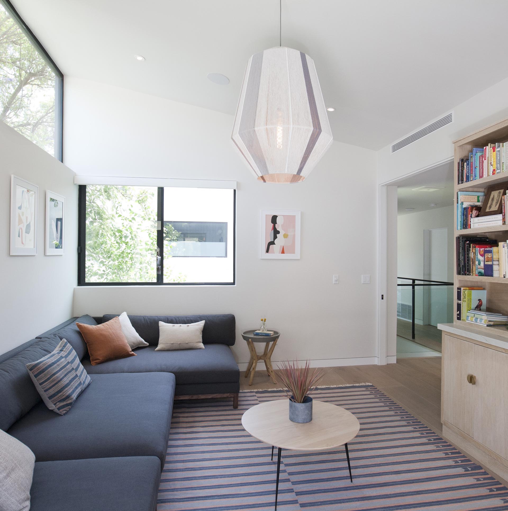 In his modern casual living / reading room, there's a dark gray sofa and a cabinet with open shelving filled with books.