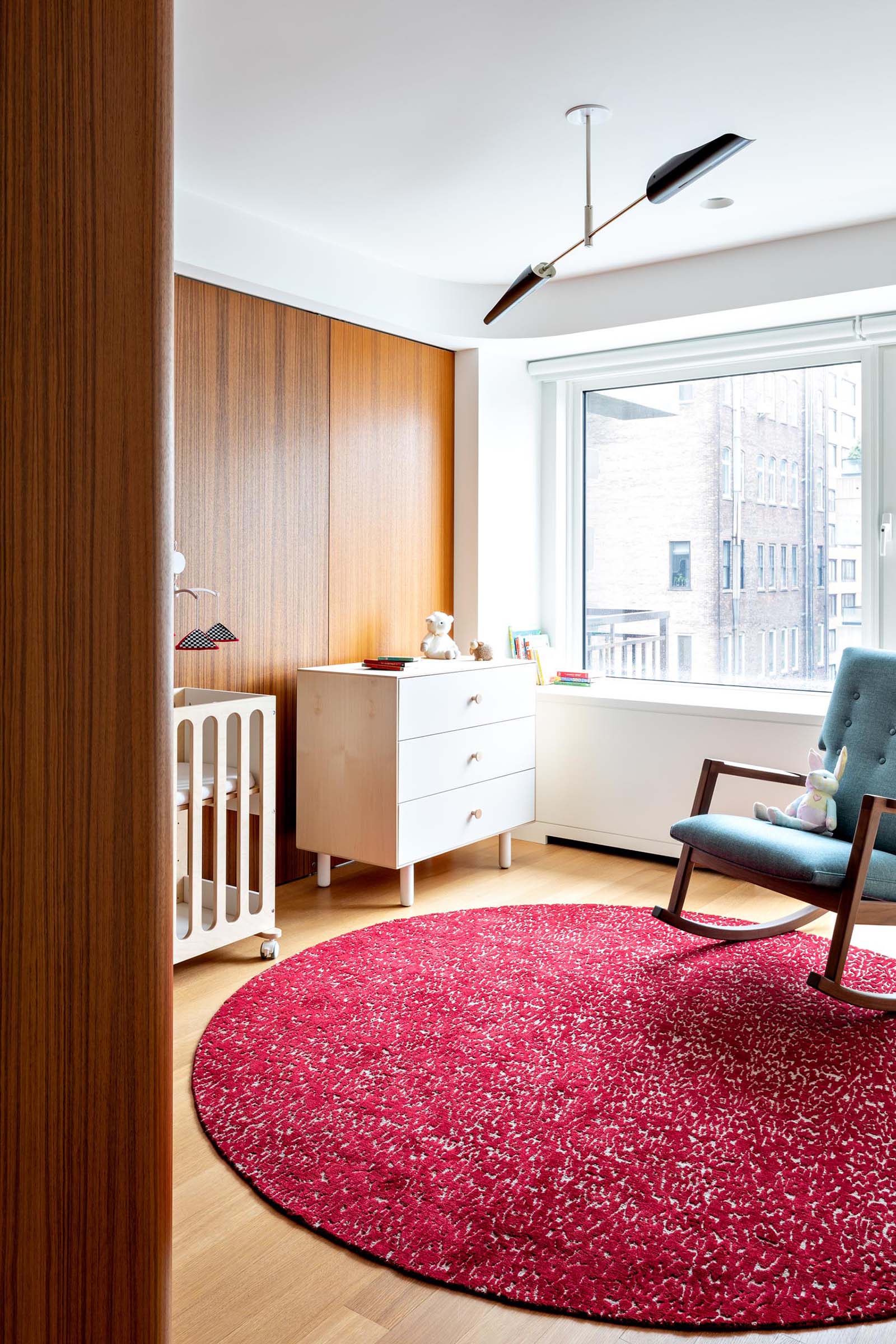 A modern nursery room with a colorful pink rug and a blue rocking chair.