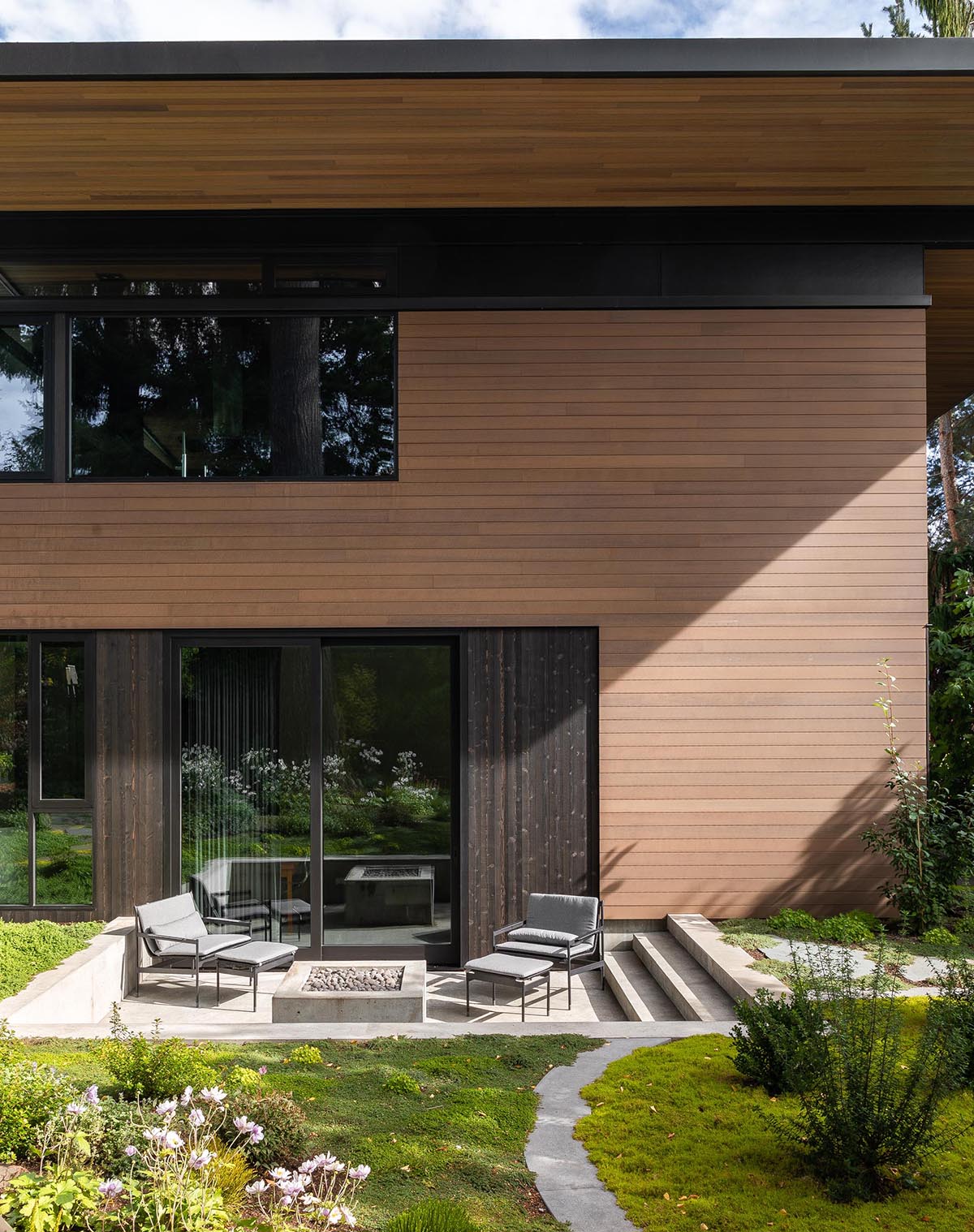 This modern home has a seating area with an outdoor fireplace, and steps that lead up to a landscaped garden.