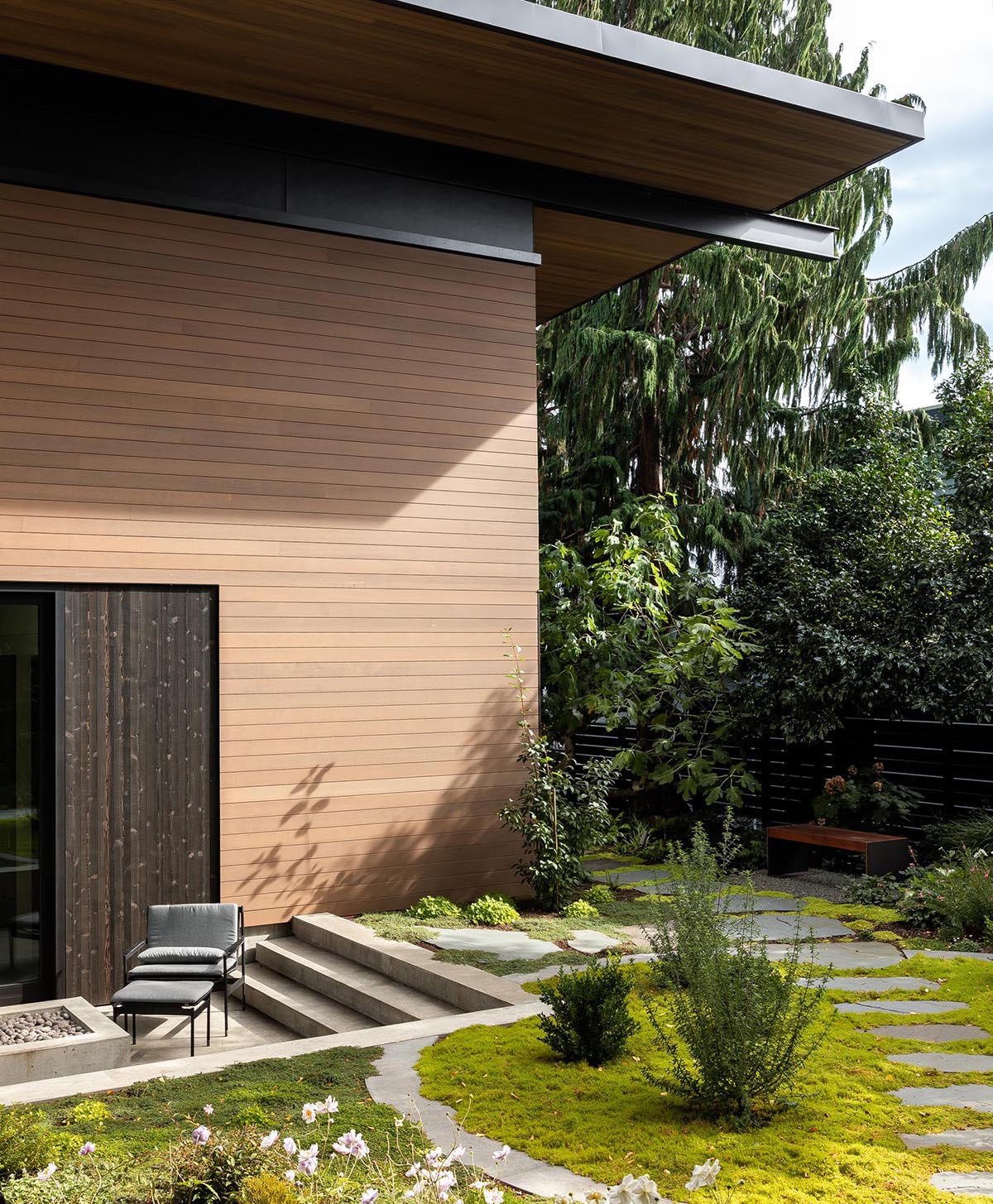 This modern home has a seating area with an outdoor fireplace, and steps that lead up to a landscaped garden.