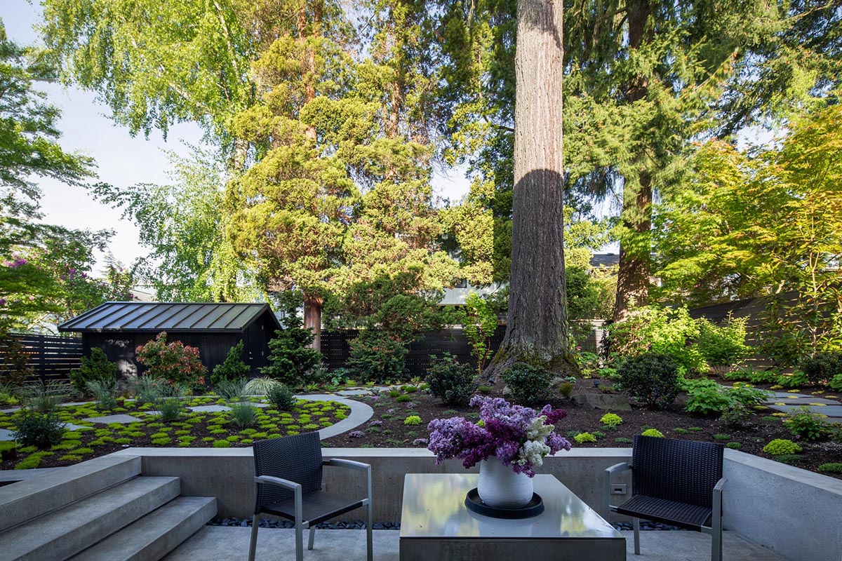 This modern home has a seating area with an outdoor fireplace, and steps that lead up to a landscaped garden.