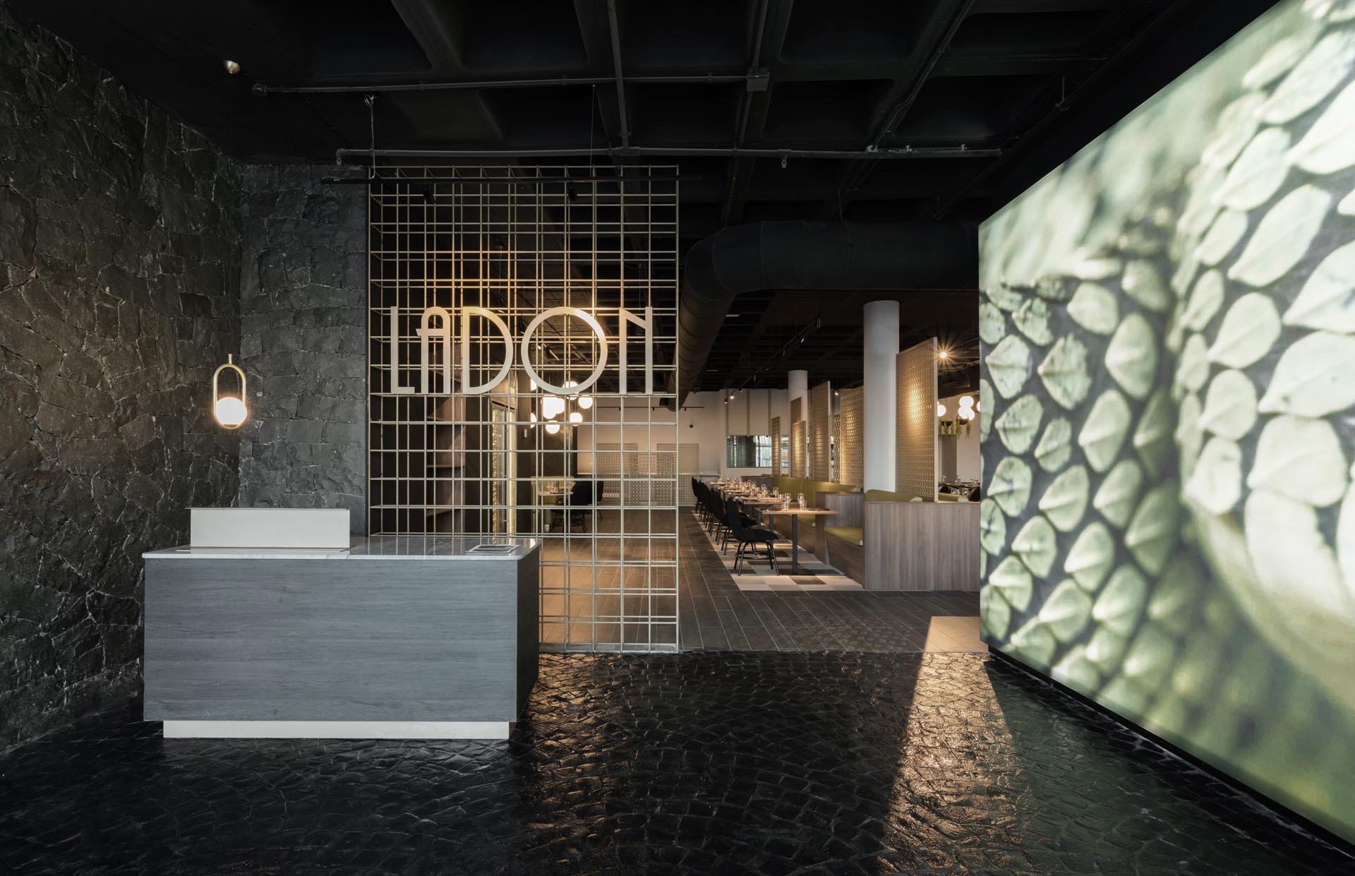 A restaurant lobby inspired by dragons with Volcanic stone walls and floors, copper structures, black ceramic scales and a large image of a dragon's skin.