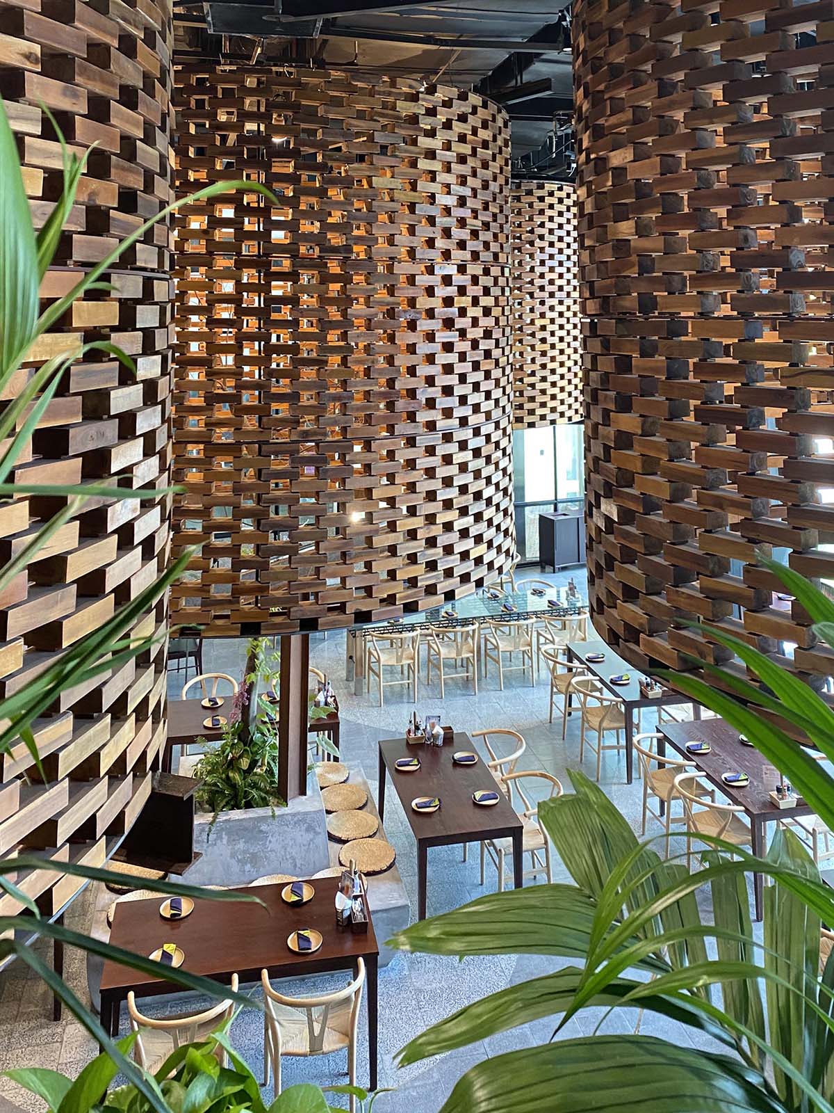 A modern restaurant interior design with large sculptural cylinders made from wood bricks, and contemporary wood furniture.