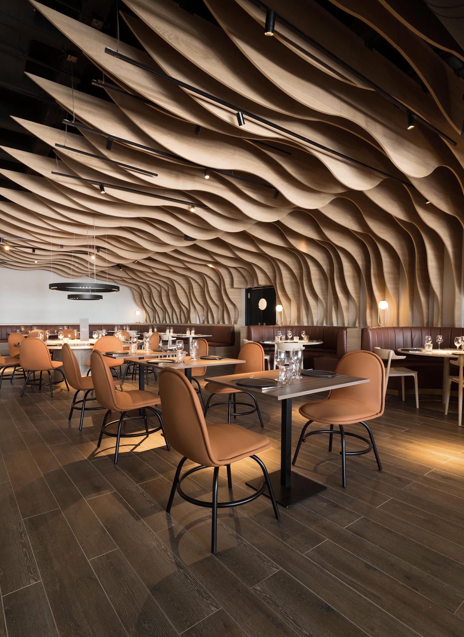 A modern restaurant with sculptural wood fins that cover the walls and ceiling, and match the surrounding furniture.