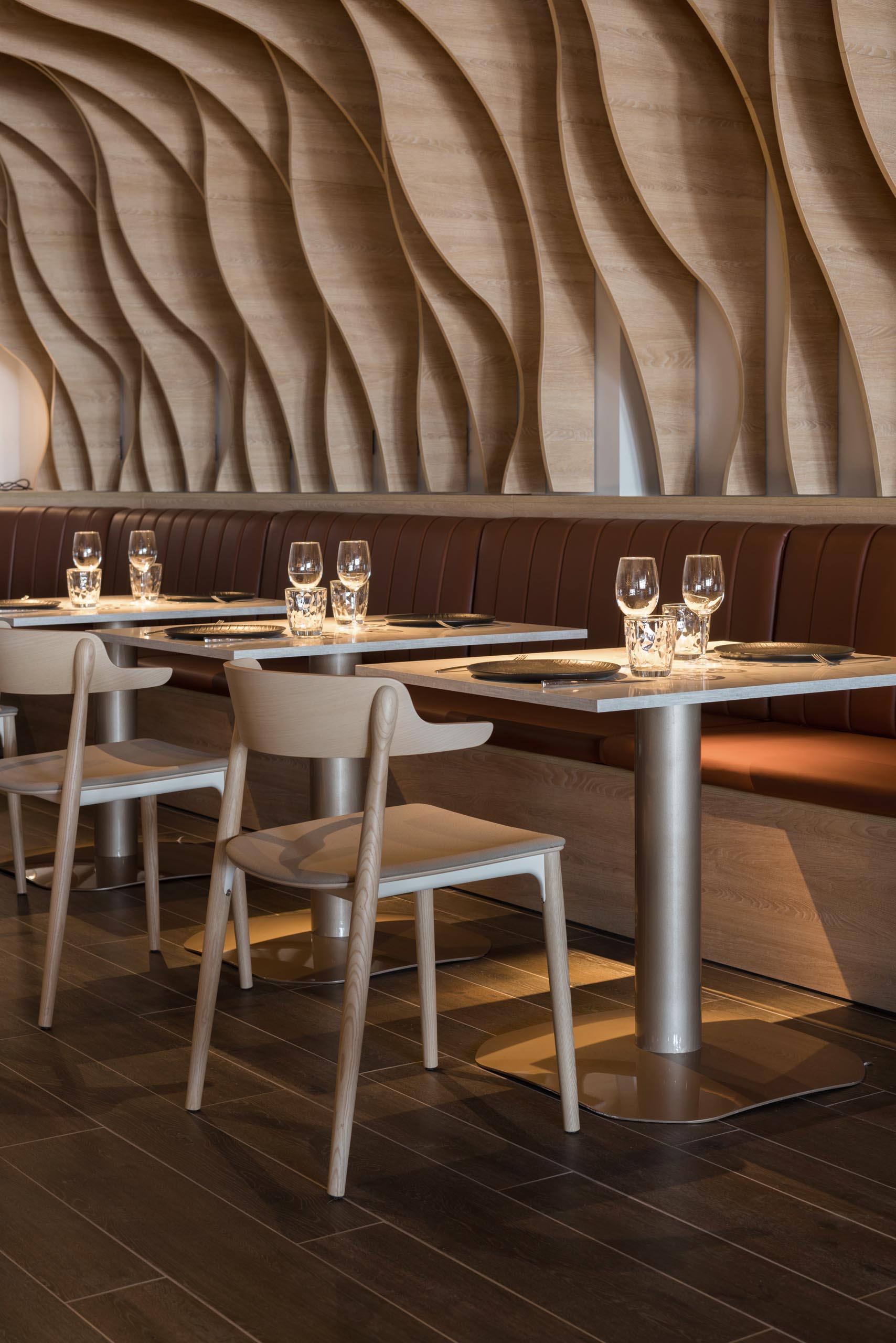 Sculptural wood fins cover the walls and ceiling, and match the surrounding furniture in a restaurant.