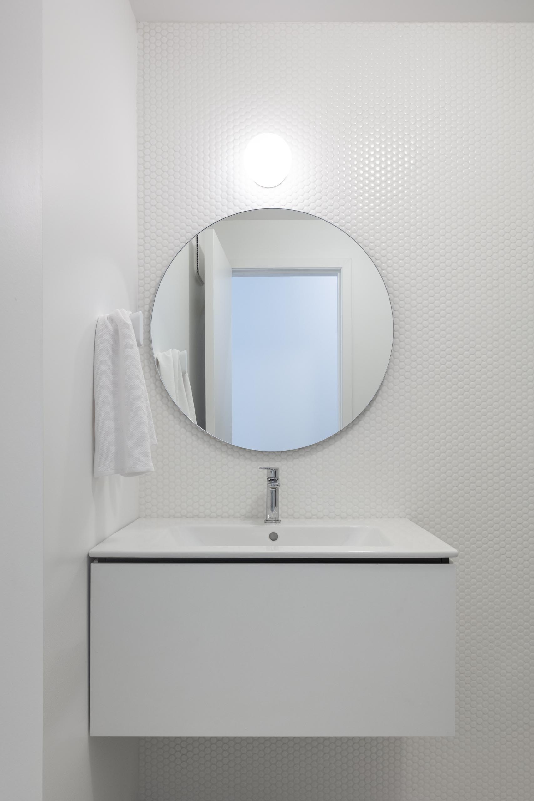 A modern white bathroom with white penny tiles and round mirror.