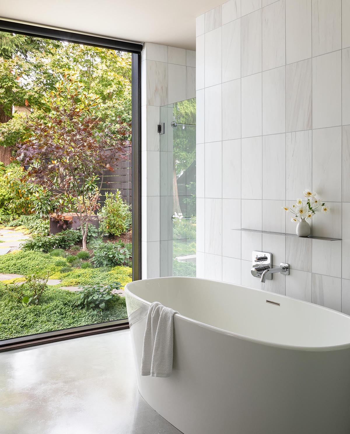 In this modern master bathroom, white tiles provide a backdrop for a freestanding bathtub and a walk-in shower.