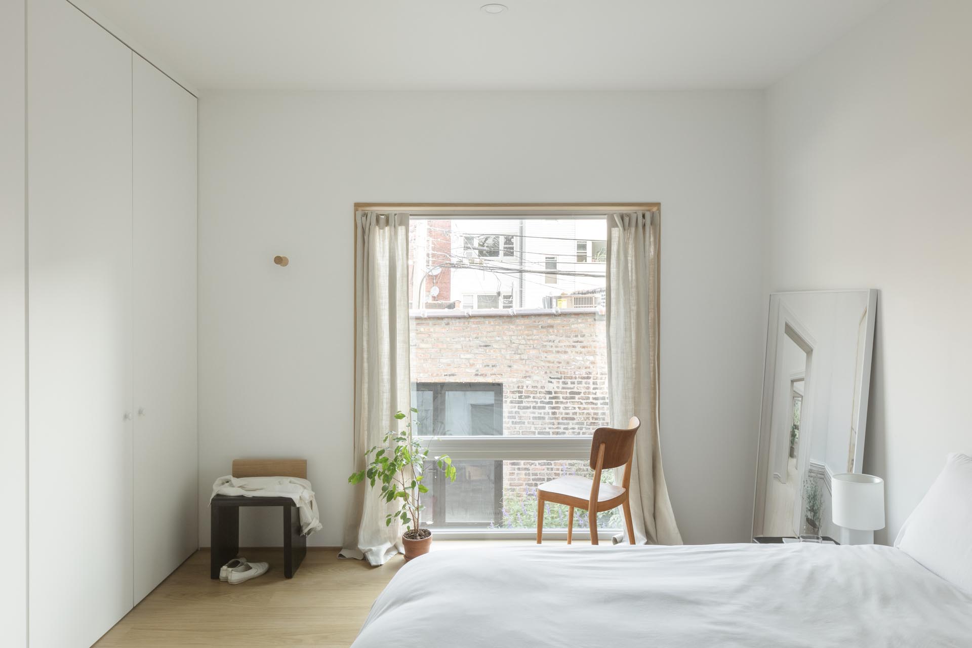 In this bedroom, minimal furnishings match the white interior, while the wood window frame complements the wood flooring.