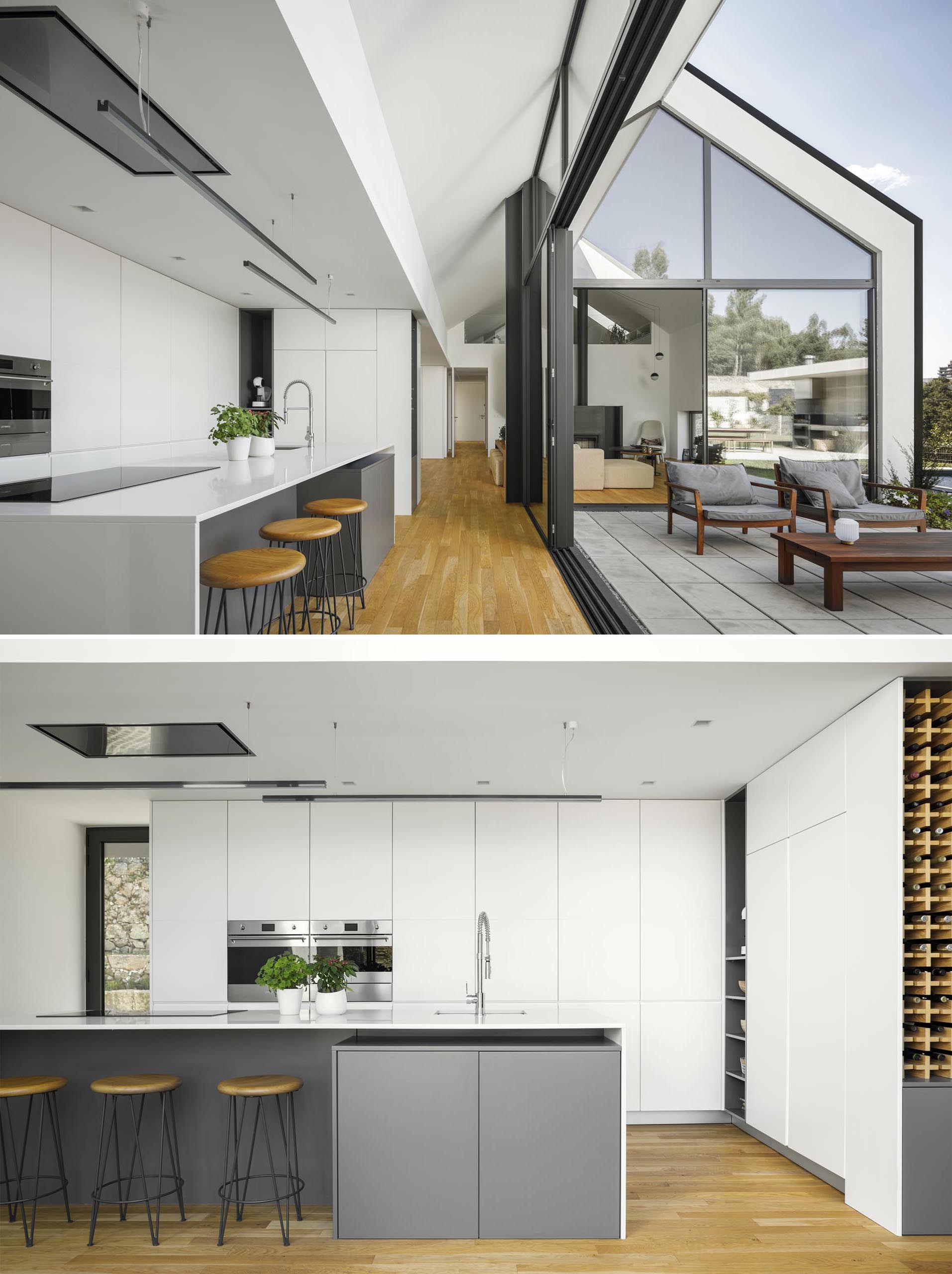 In this modern kitchen, minimalist white cabinets have been paired with white countertops, linear suspension lights, and an island with a gray base. 