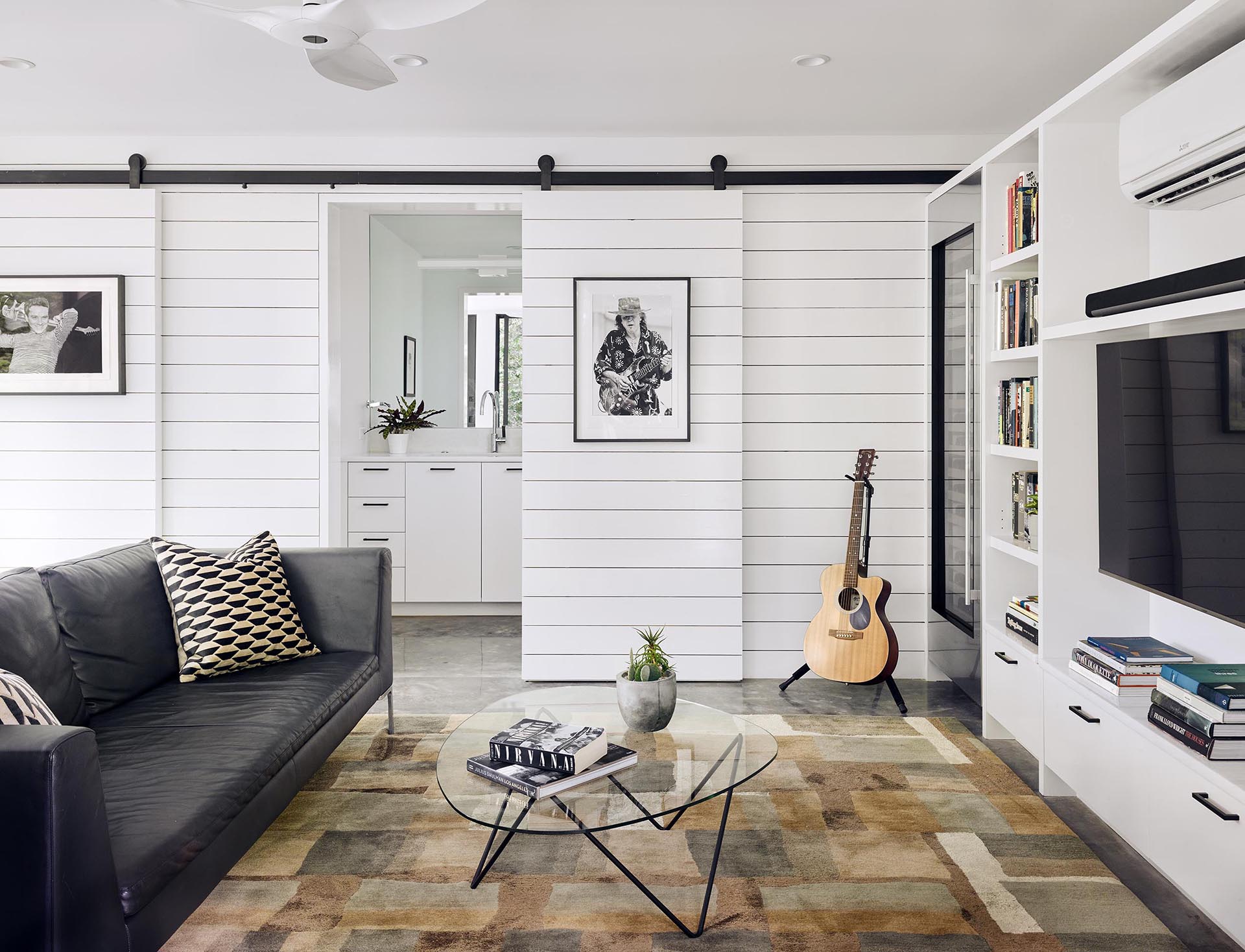 A modern living room with white walls, sliding barn doors, and a custom shelving unit that surrounds a television.