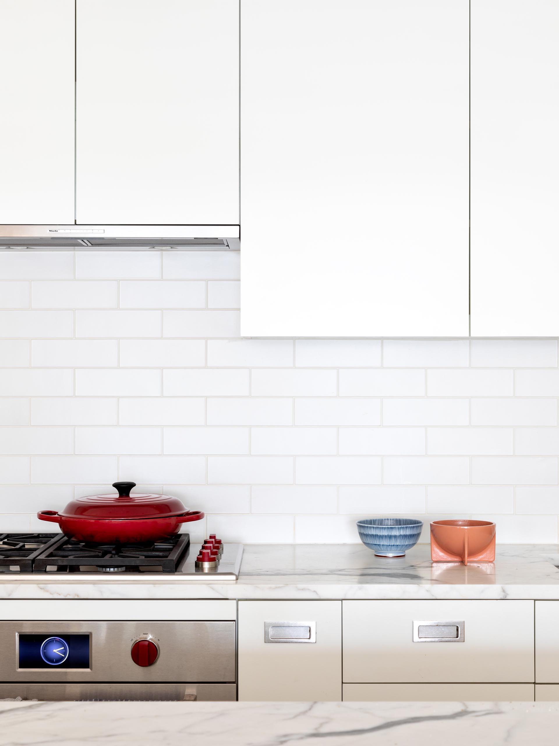 A modern kitchen has been kept bright with modern white cabinets, integrated appliances, and subway tiles, and a matching island. 