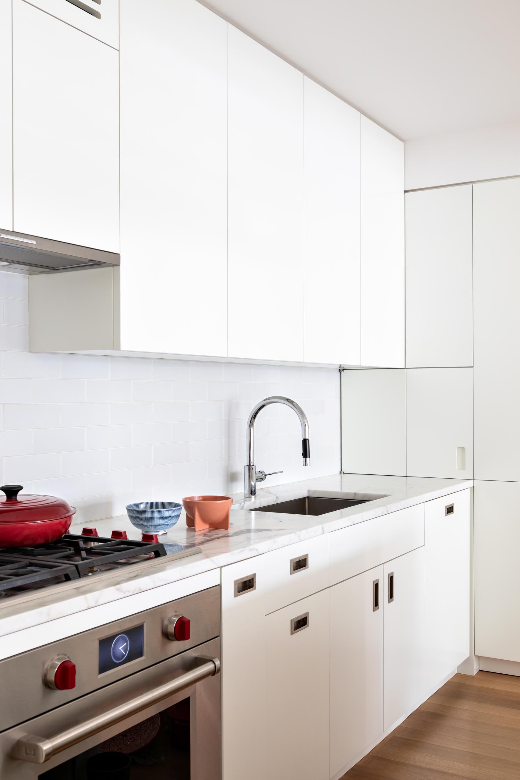 A modern kitchen has been kept bright with modern white cabinets, integrated appliances, and subway tiles, and a matching island. 
