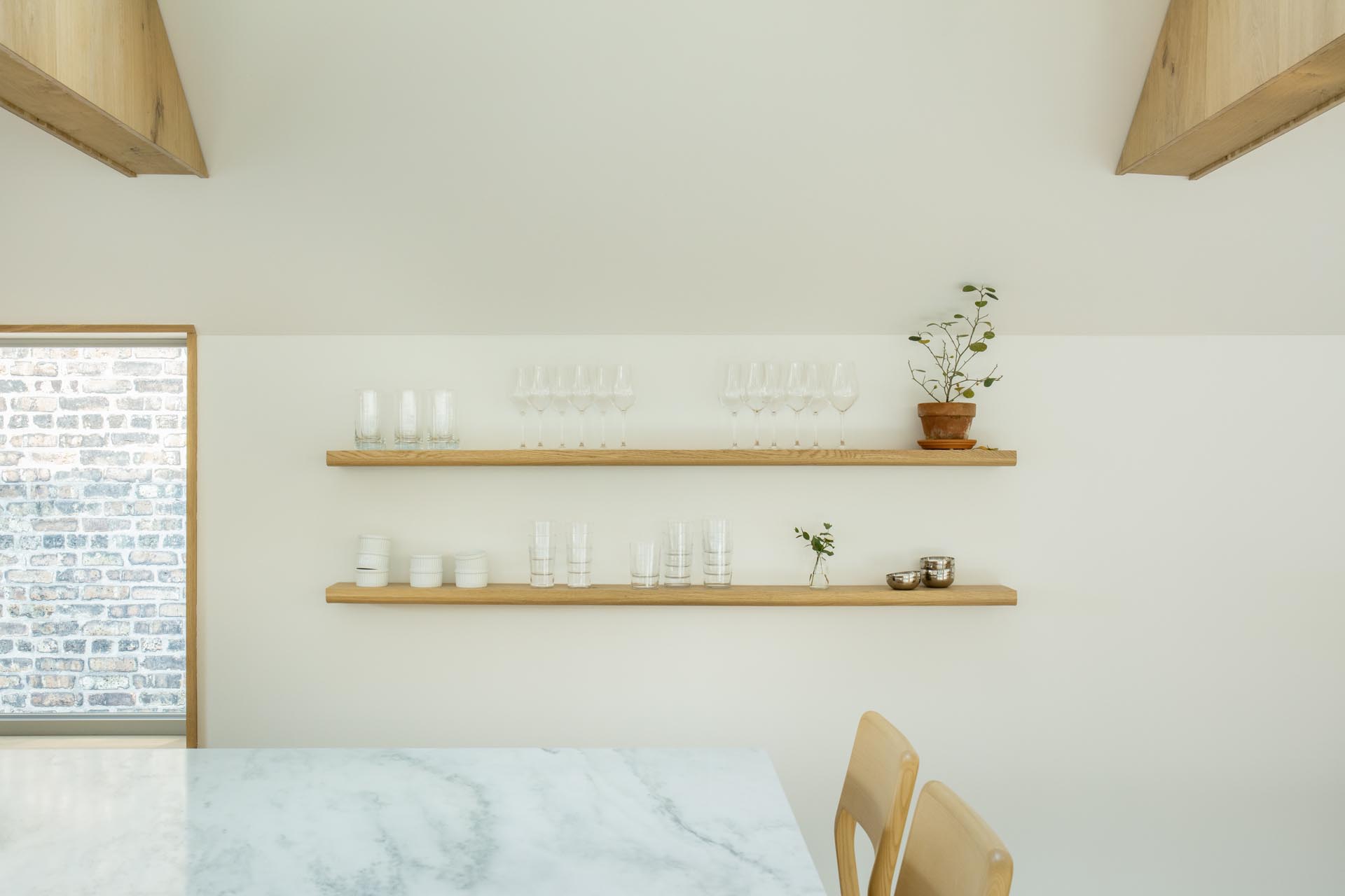 This modern kitchen has floating wood shelves, white countertops, and an island with seating. 