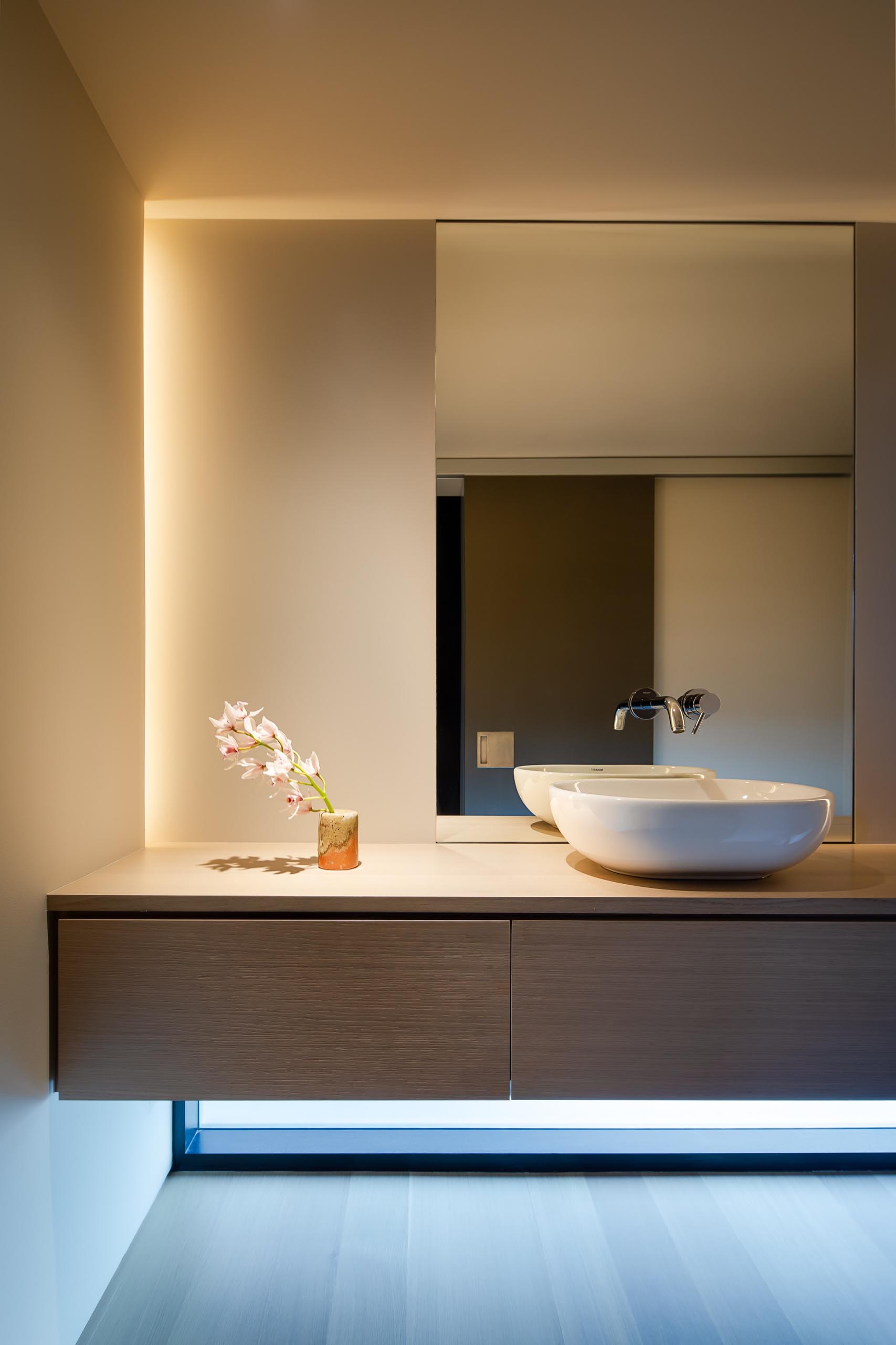 In this modern bathroom, there's a floating wood vanity with hidden lighting tucked away in the corner.