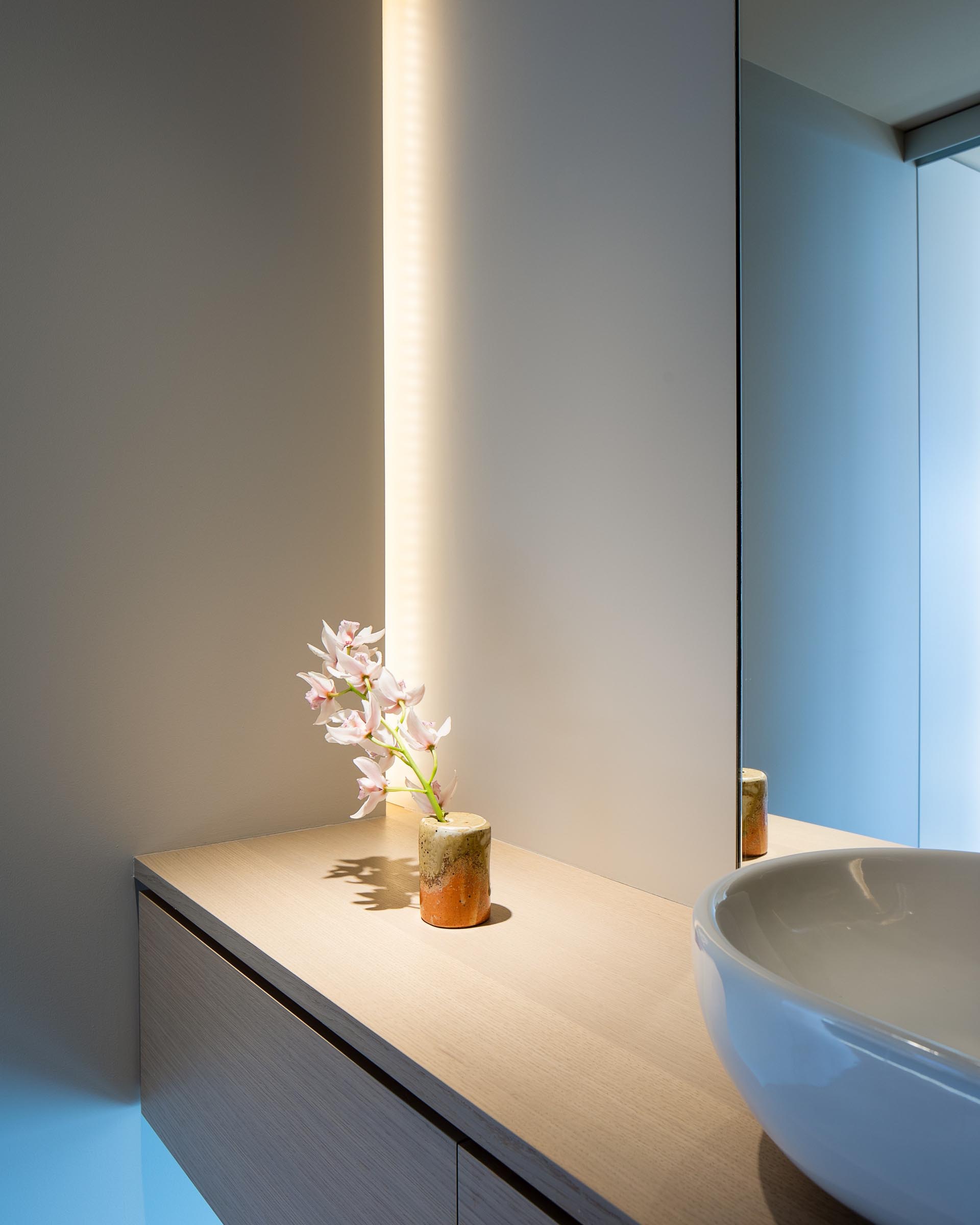 In this modern bathroom, there's a floating wood vanity with hidden lighting tucked away in the corner.