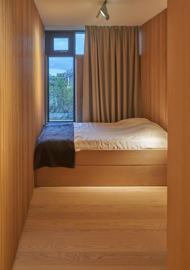 A modern bedroom lined with wood that has a built-in bed.